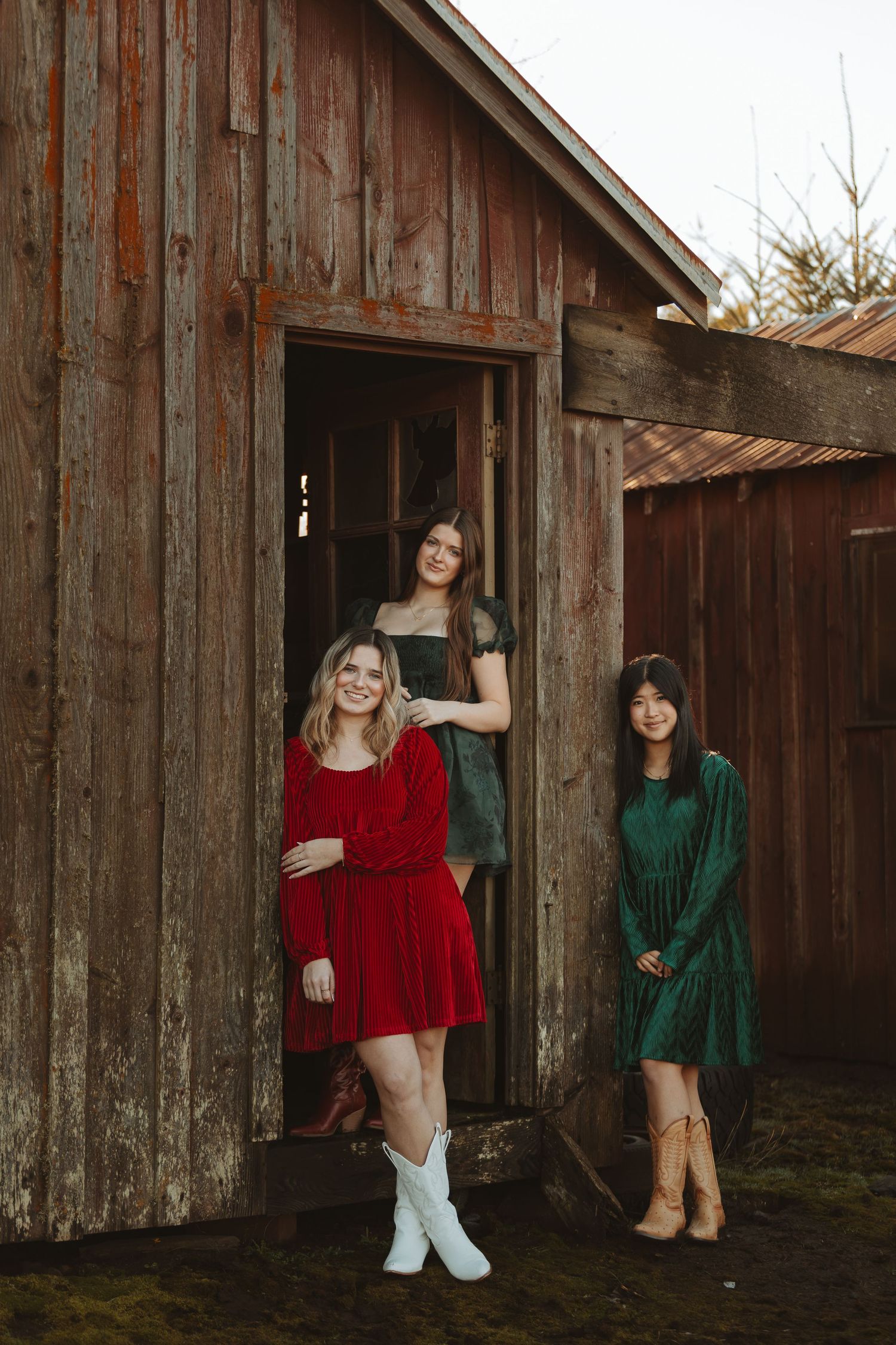 Three people in festive dresses pose by rustic barn door wearing contrasting boots.
