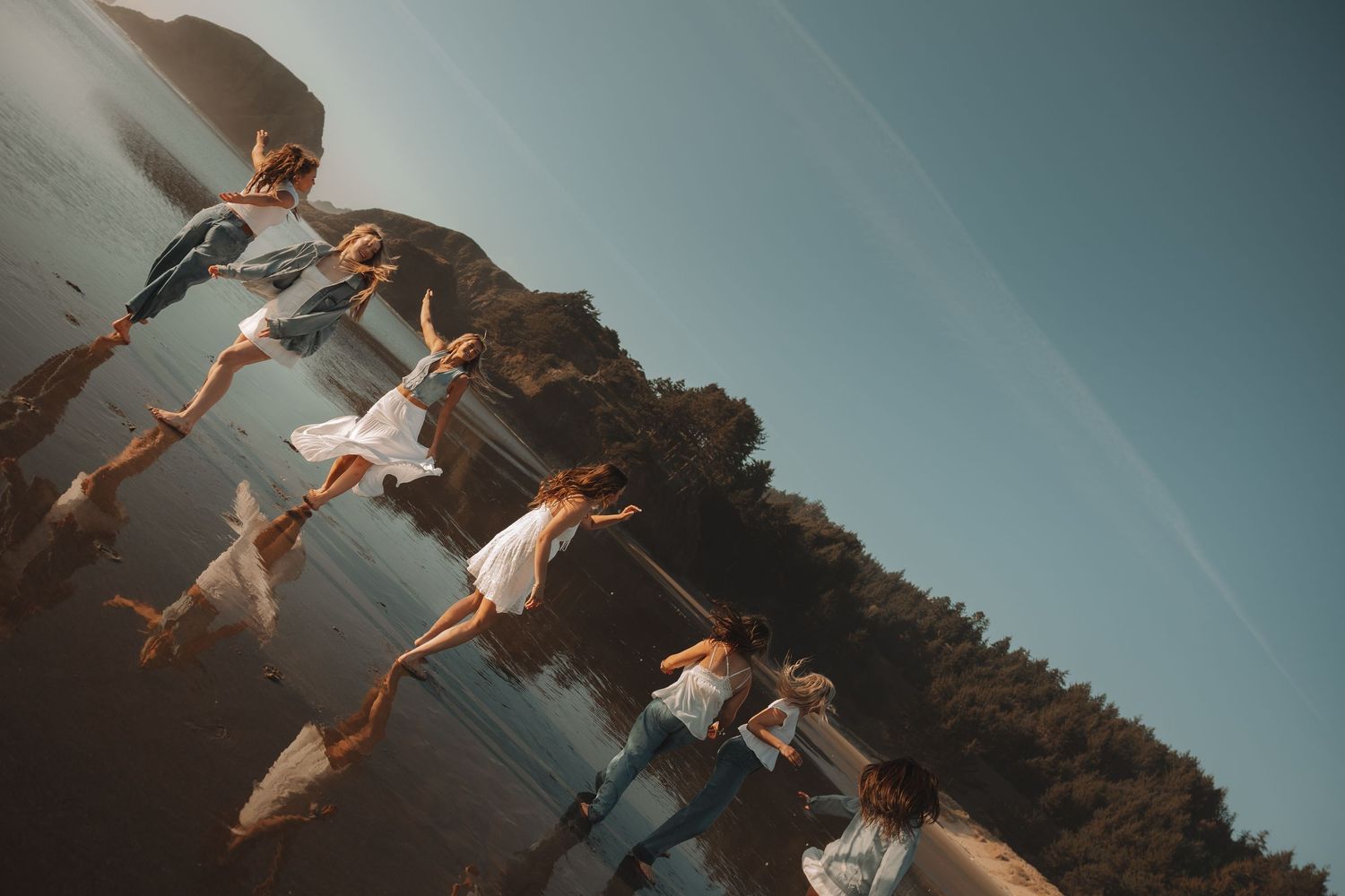 Creative upside-down reflection photo of women in white and denim on a beach shoreline.
