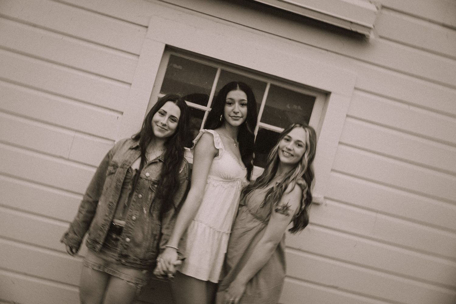 Group poses casually in vintage-style black and white photo against building wall.