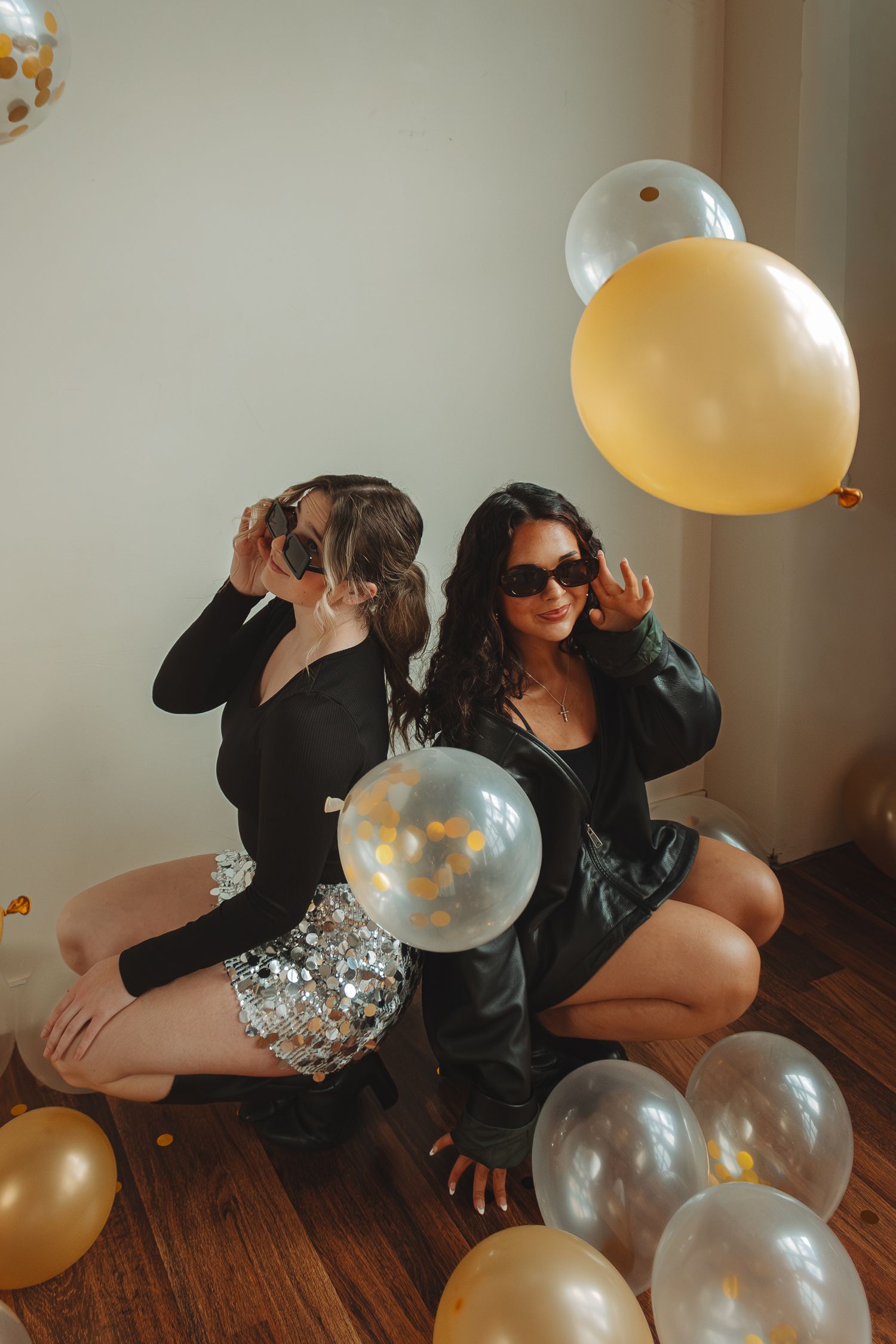 Two people pose with silver and gold balloons on wooden floor in artistic shoot.