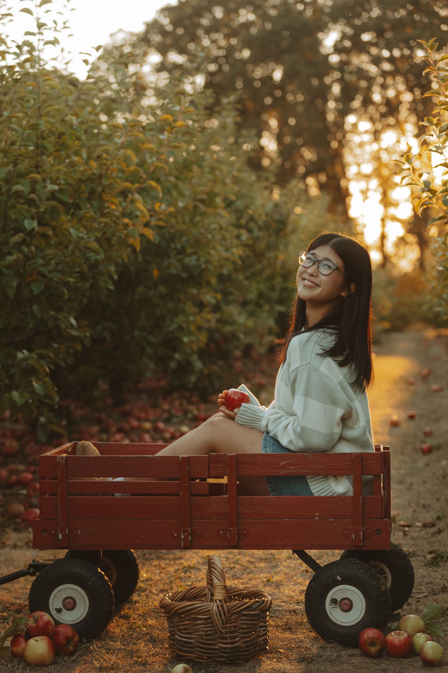 Person relaxing on wooden bench at sunset with apples and wicker baskets in autumn garden setting.