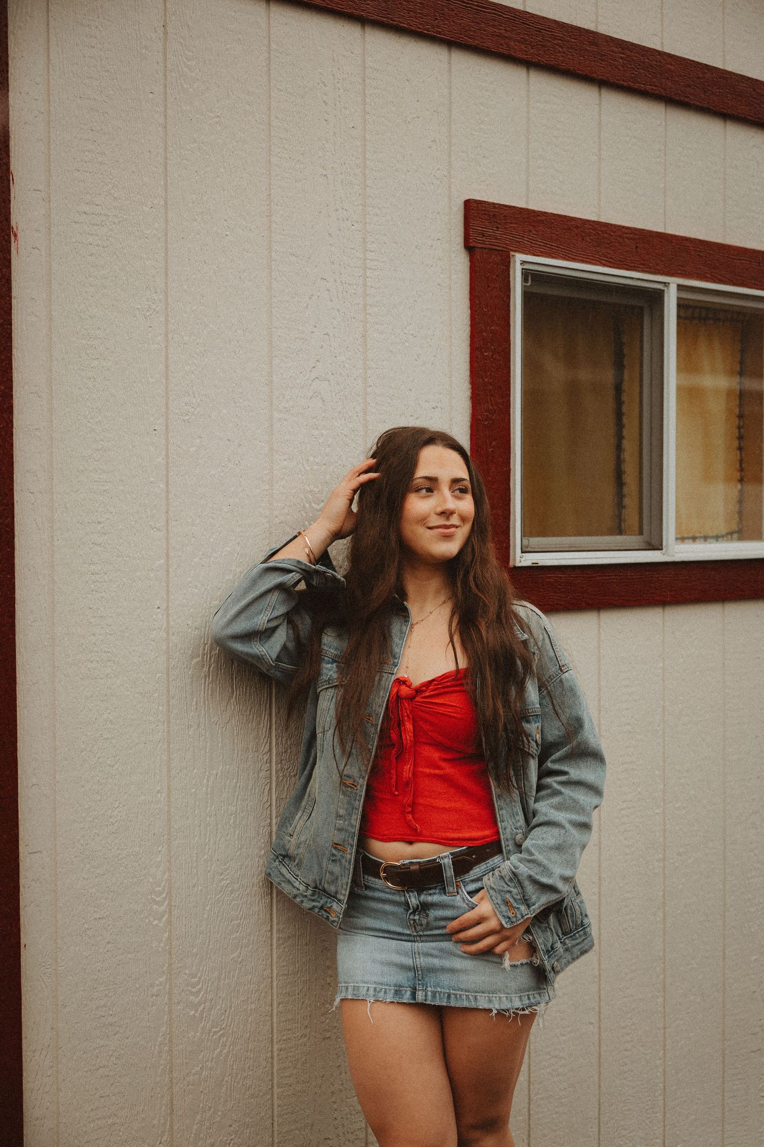 Casual denim and red top combination photographed against neutral building exterior.