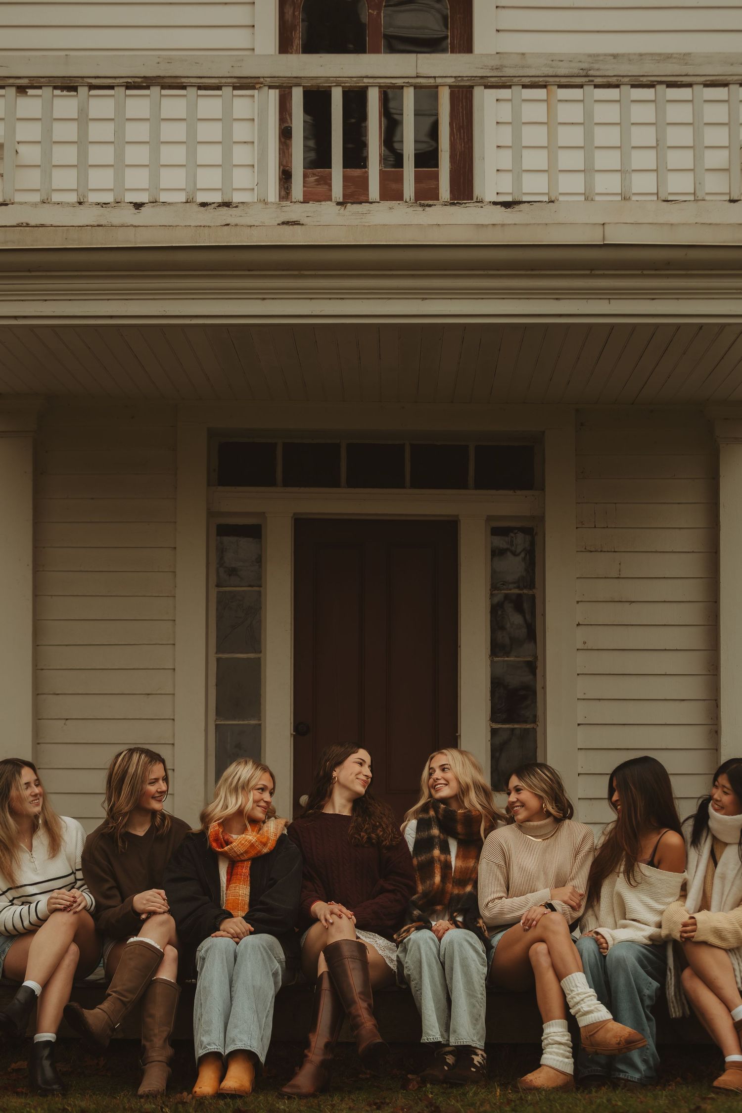 A group of friends sit casually together on a white porch during golden hour.
