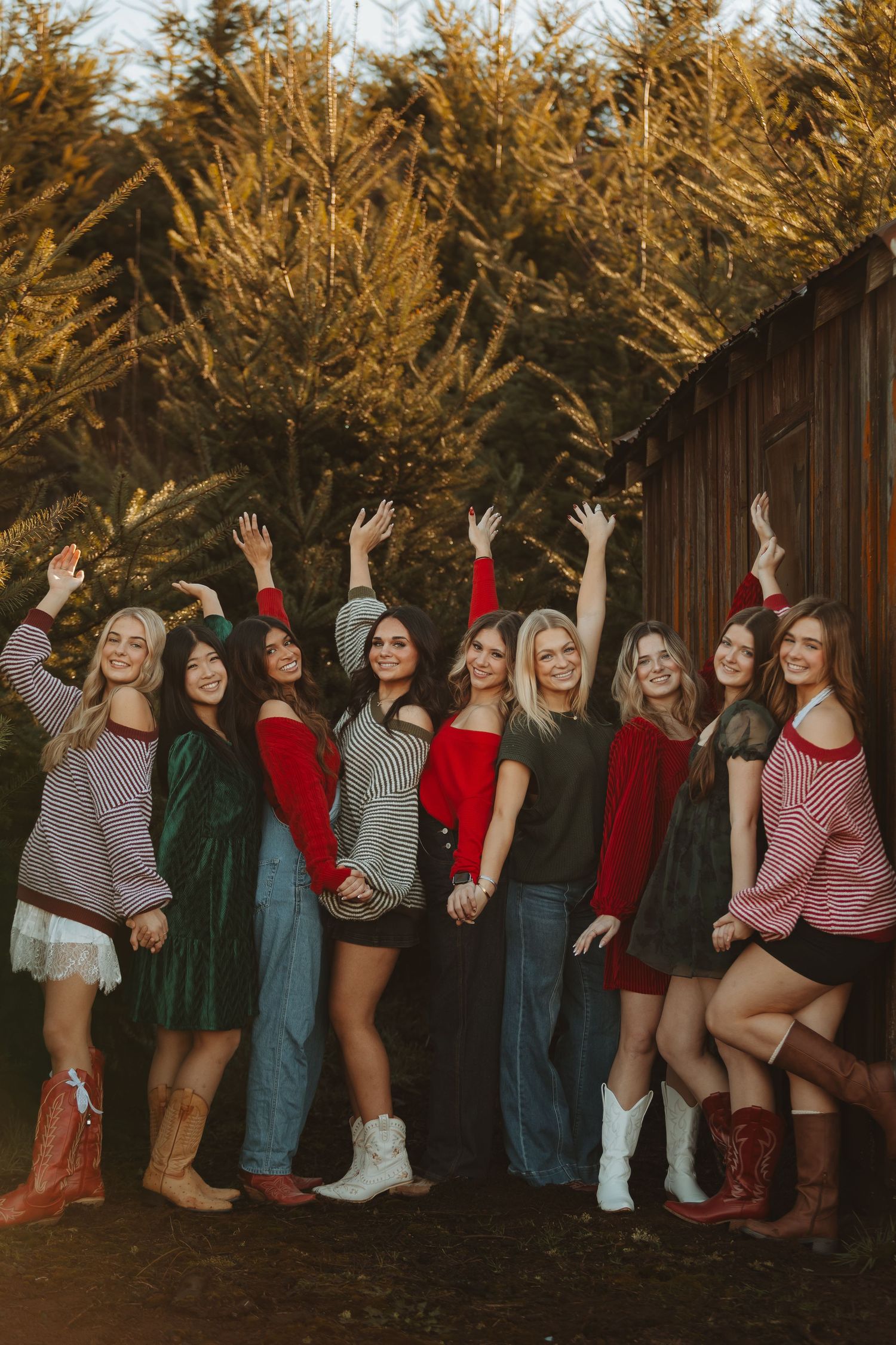Friends line up against wooden wall wearing mix of casual and western-inspired outfits for group photo.
