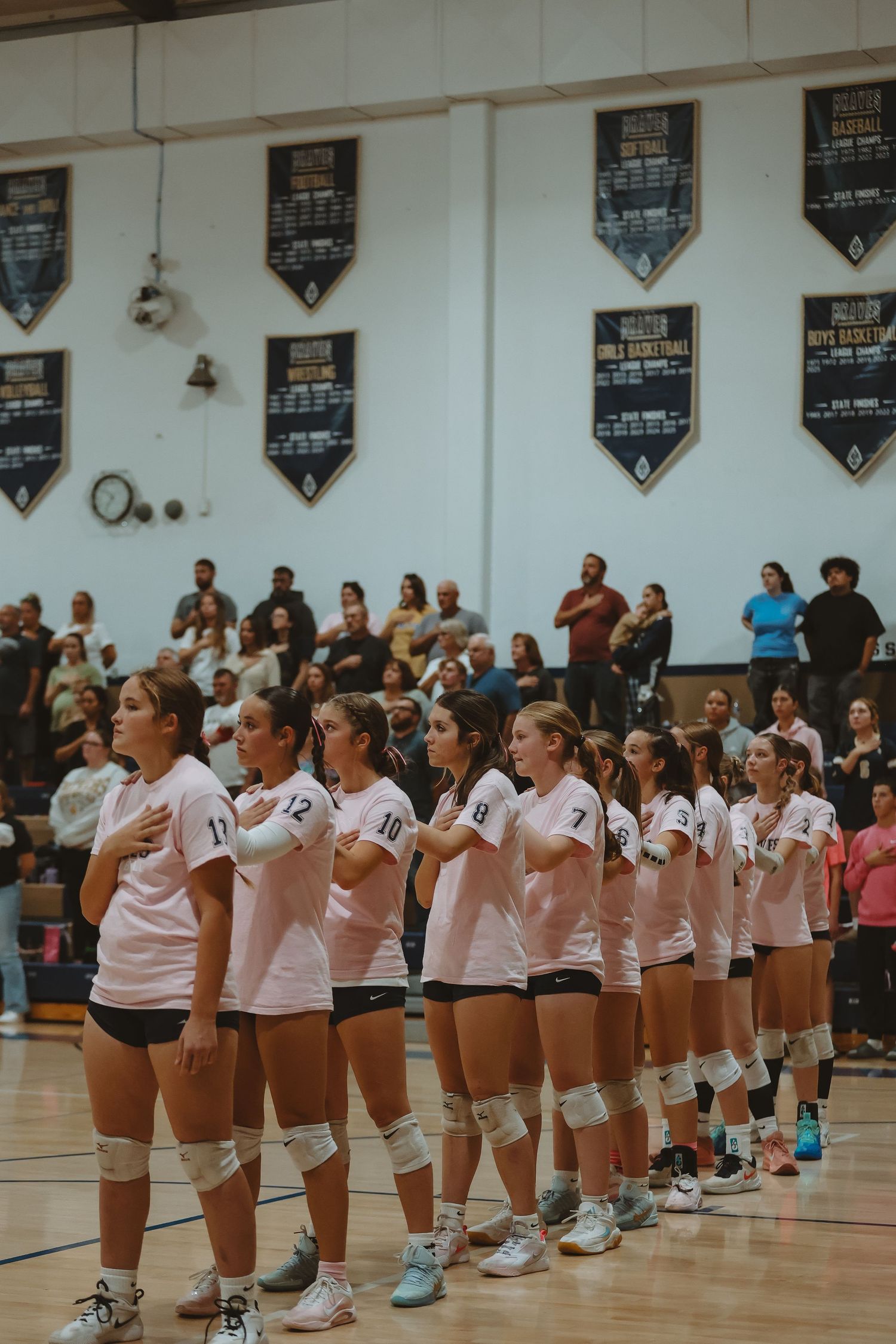 A volleyball team lines up on the sideline of a gymnasium court during a pre-game ceremony.