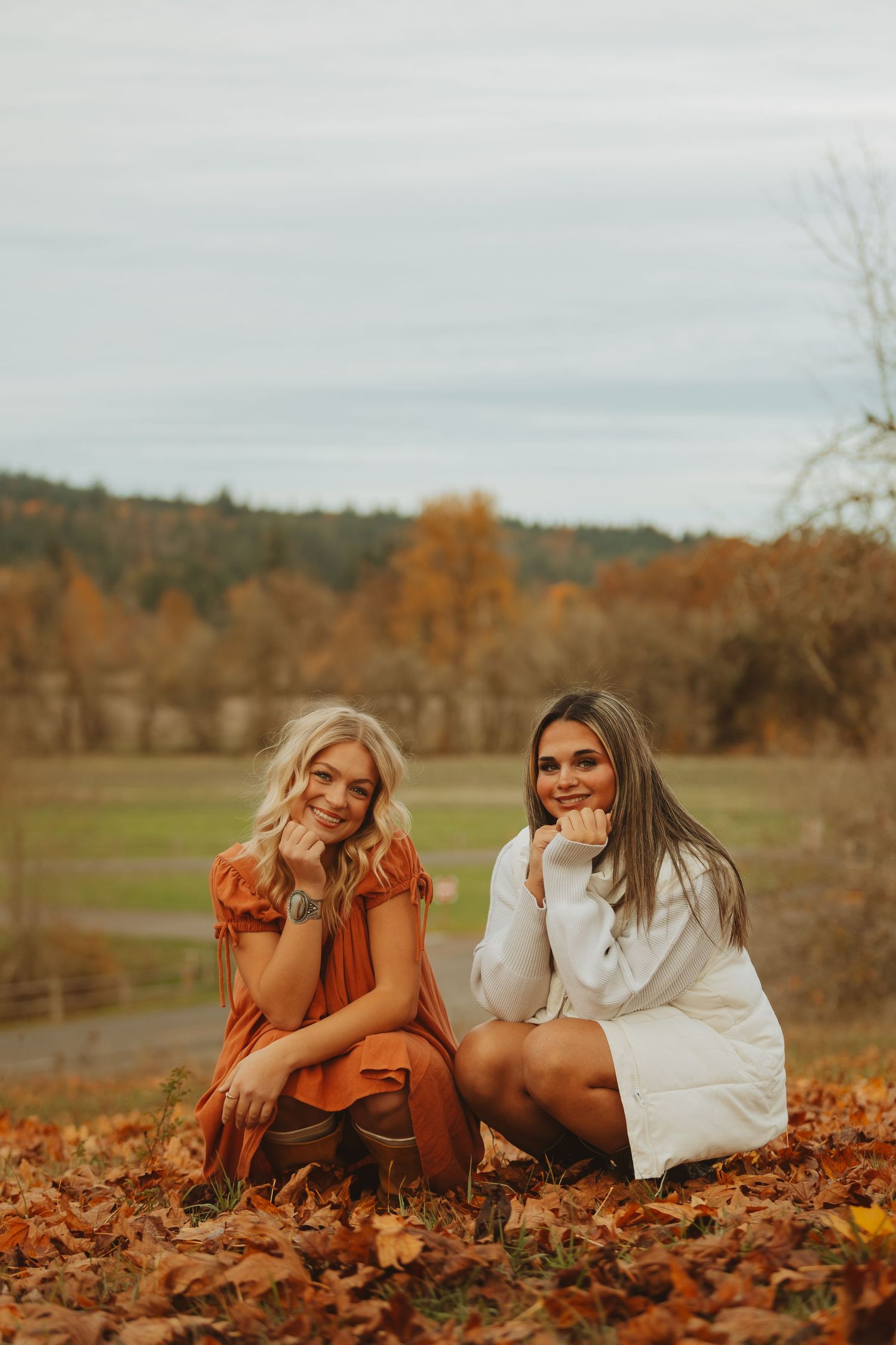 Friends laying in autumn leaves during a fall photoshoot in a rustic outdoor setting.