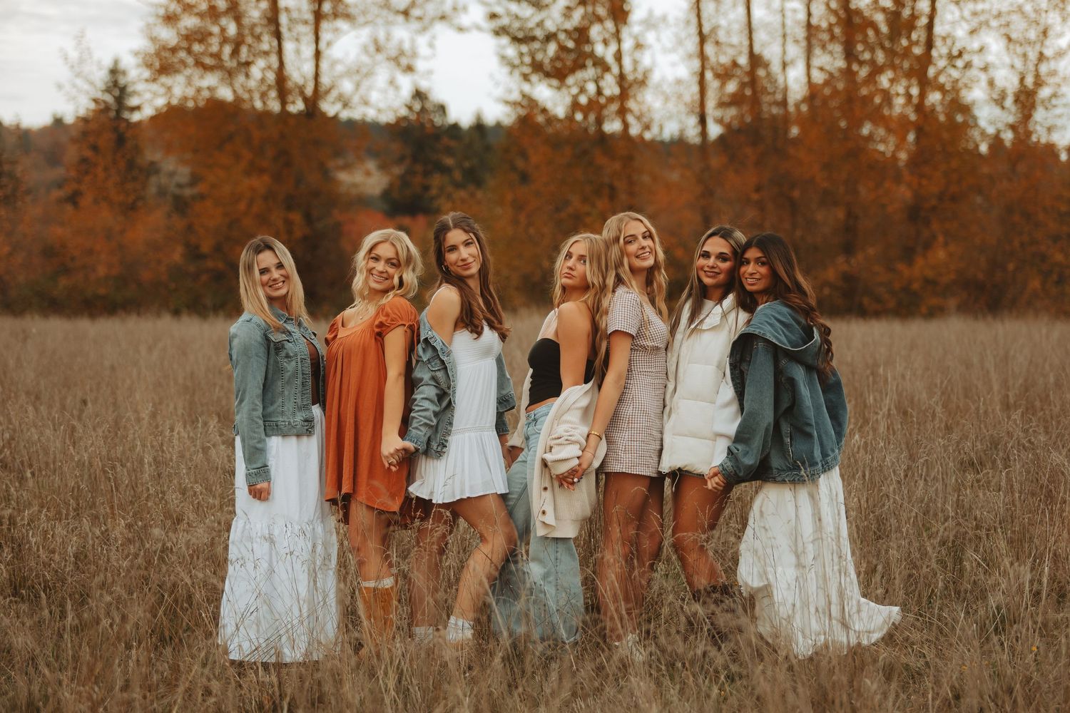 Group photo in coordinated autumn outfits standing together in a rustic field at sunset.