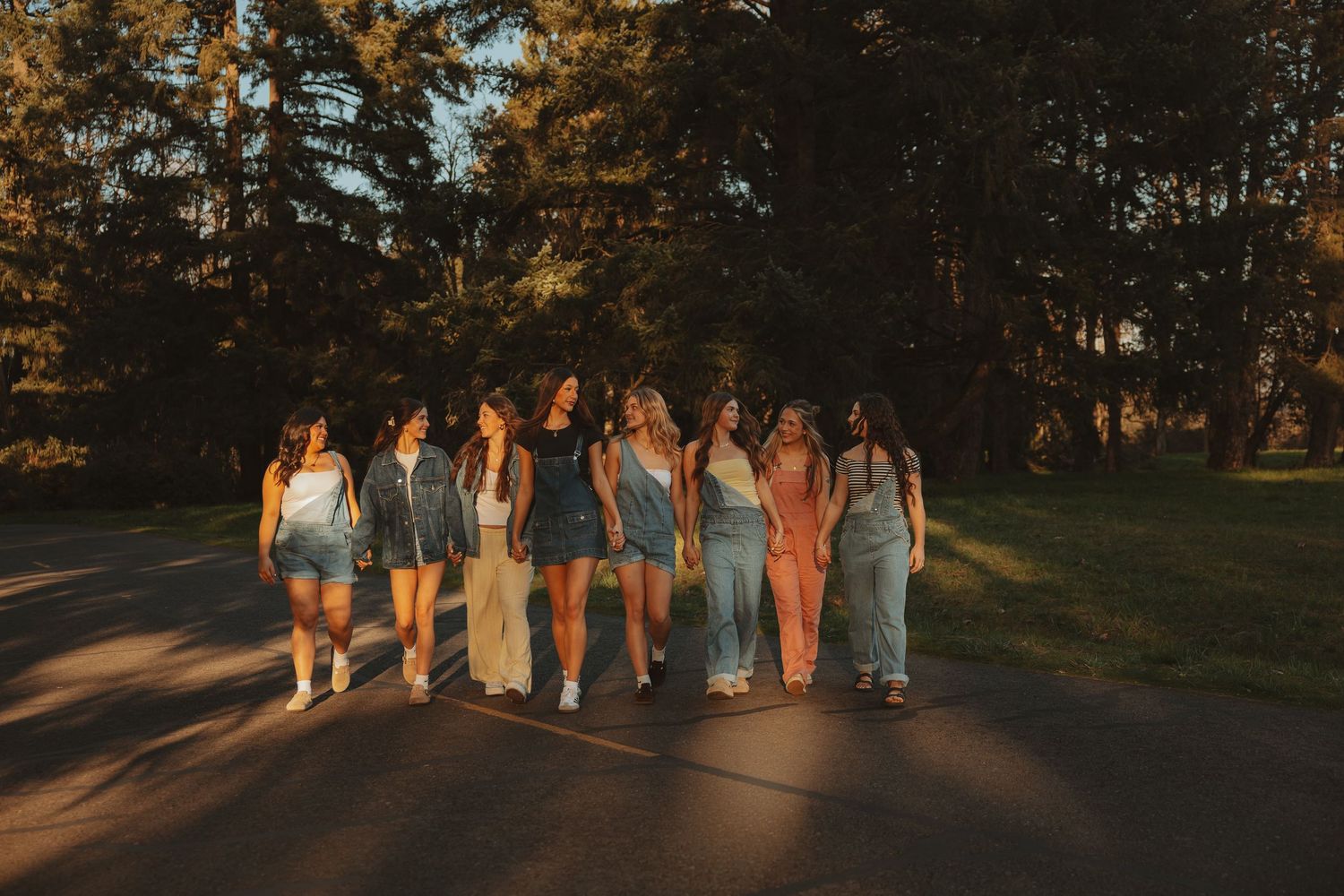 A group of women walking together on a sunlit road surrounded by lush green trees during golden hour.