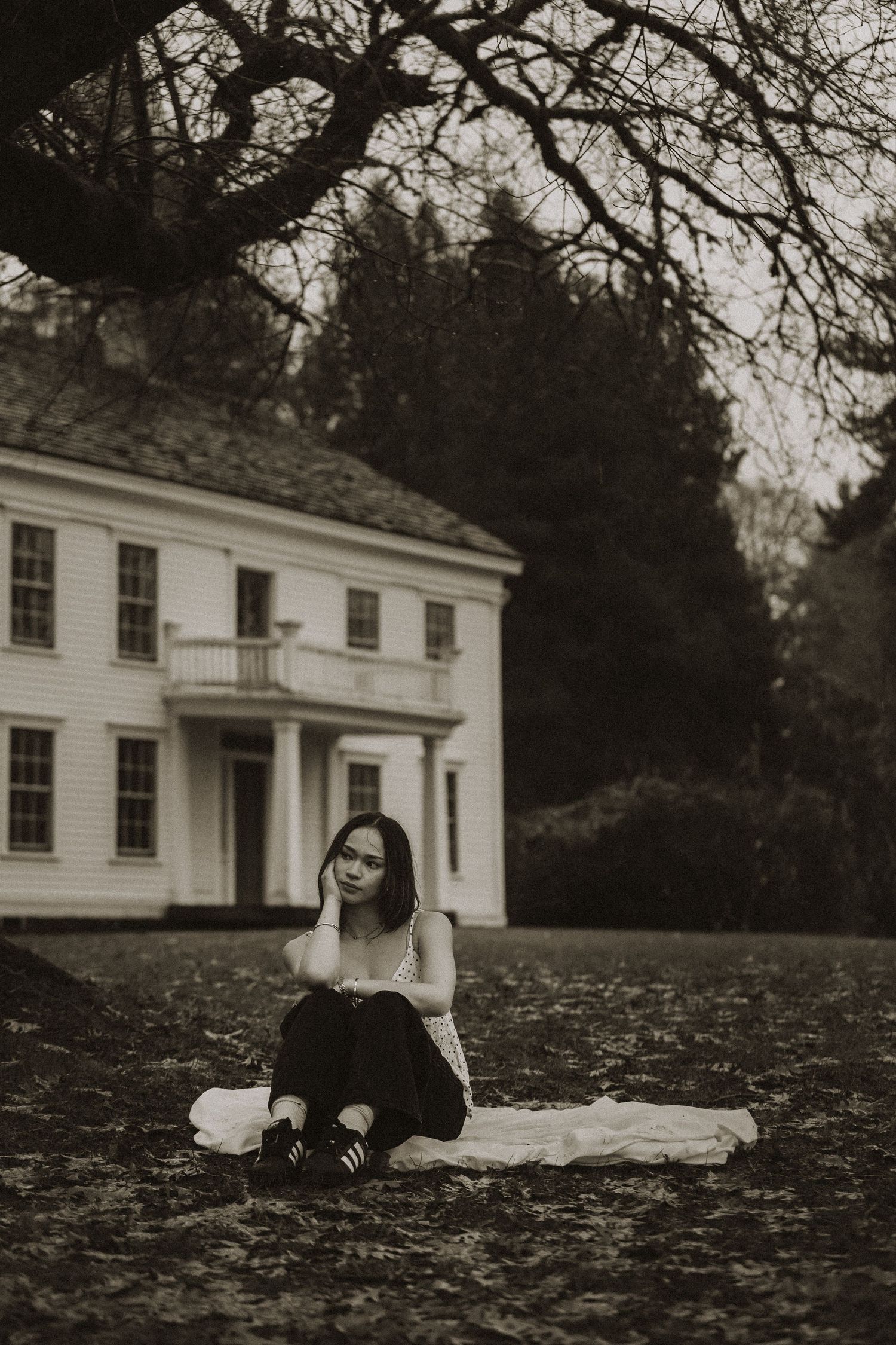 Black and white photo series showing a person lying in fallen leaves near a white colonial style house.