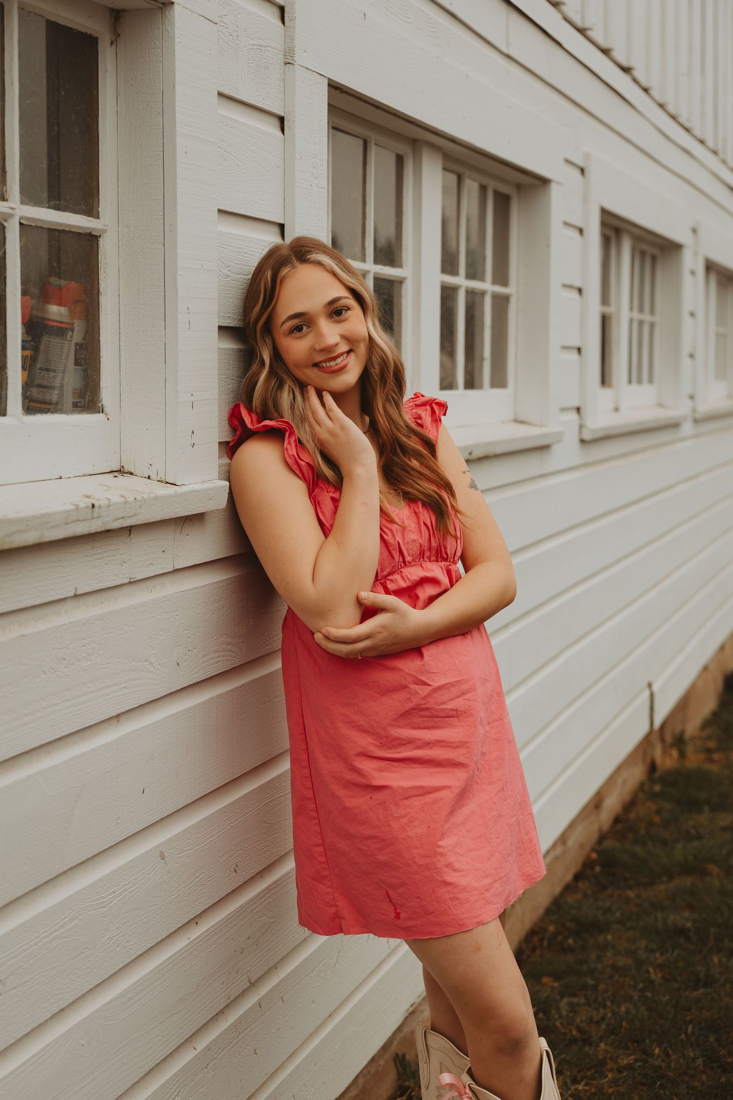 Model in coral dress poses playfully against white building exterior in casual fashion photoshoot.