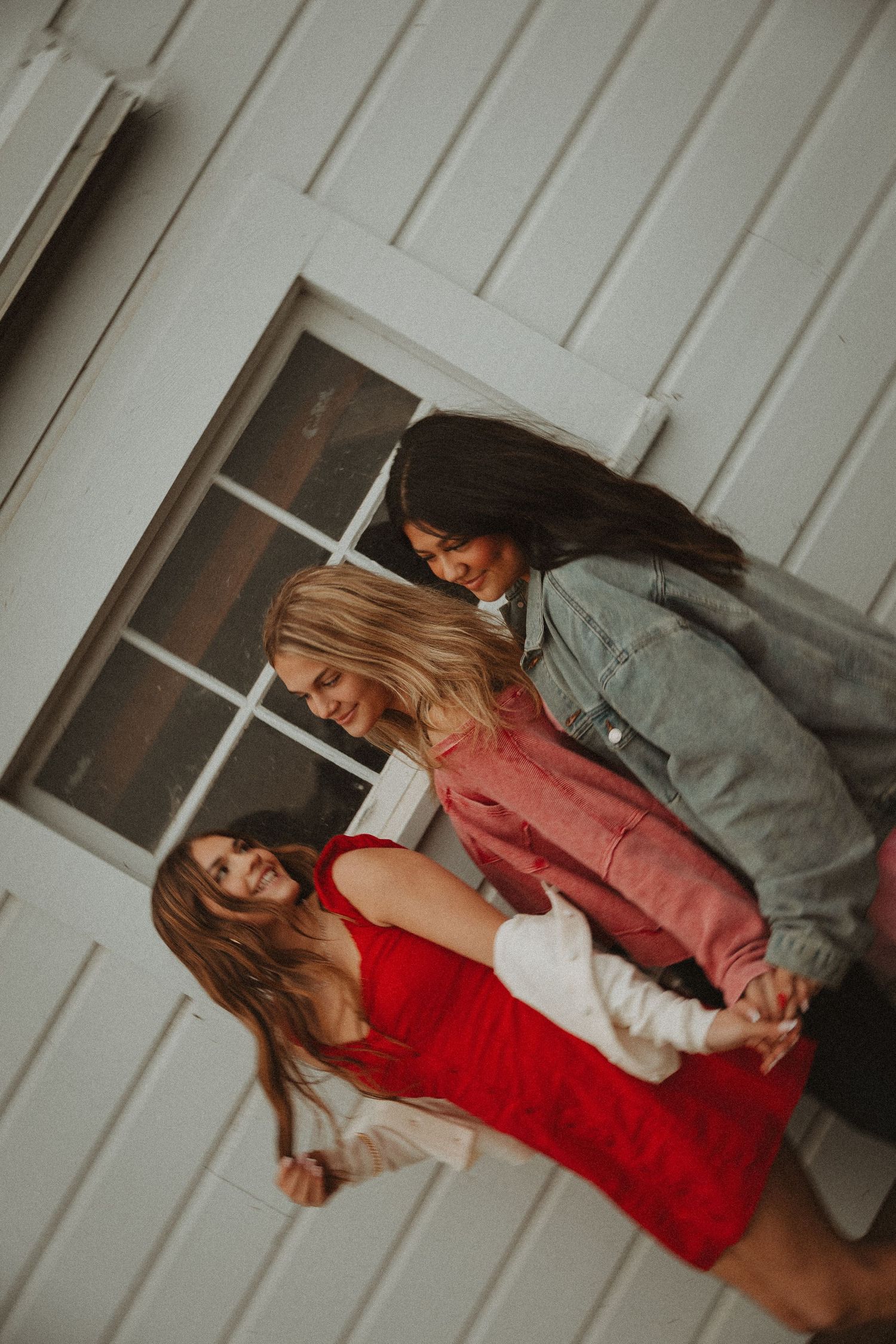 Lifestyle fashion photography featuring models in red and pink outfits against white building wall.