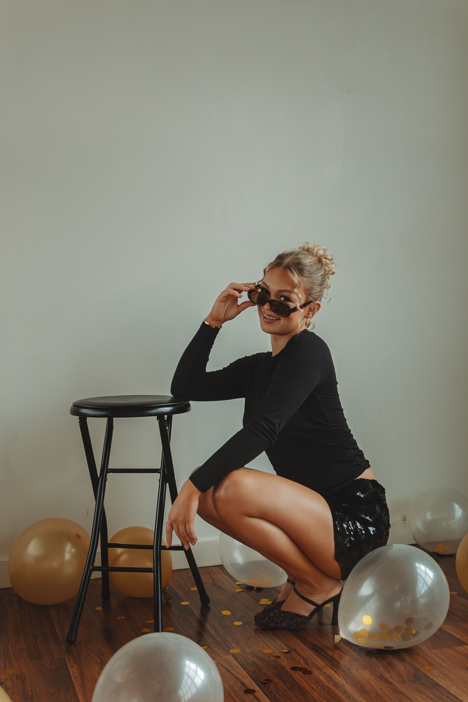 Figure in black outfit poses dramatically with balloons on wooden floor.