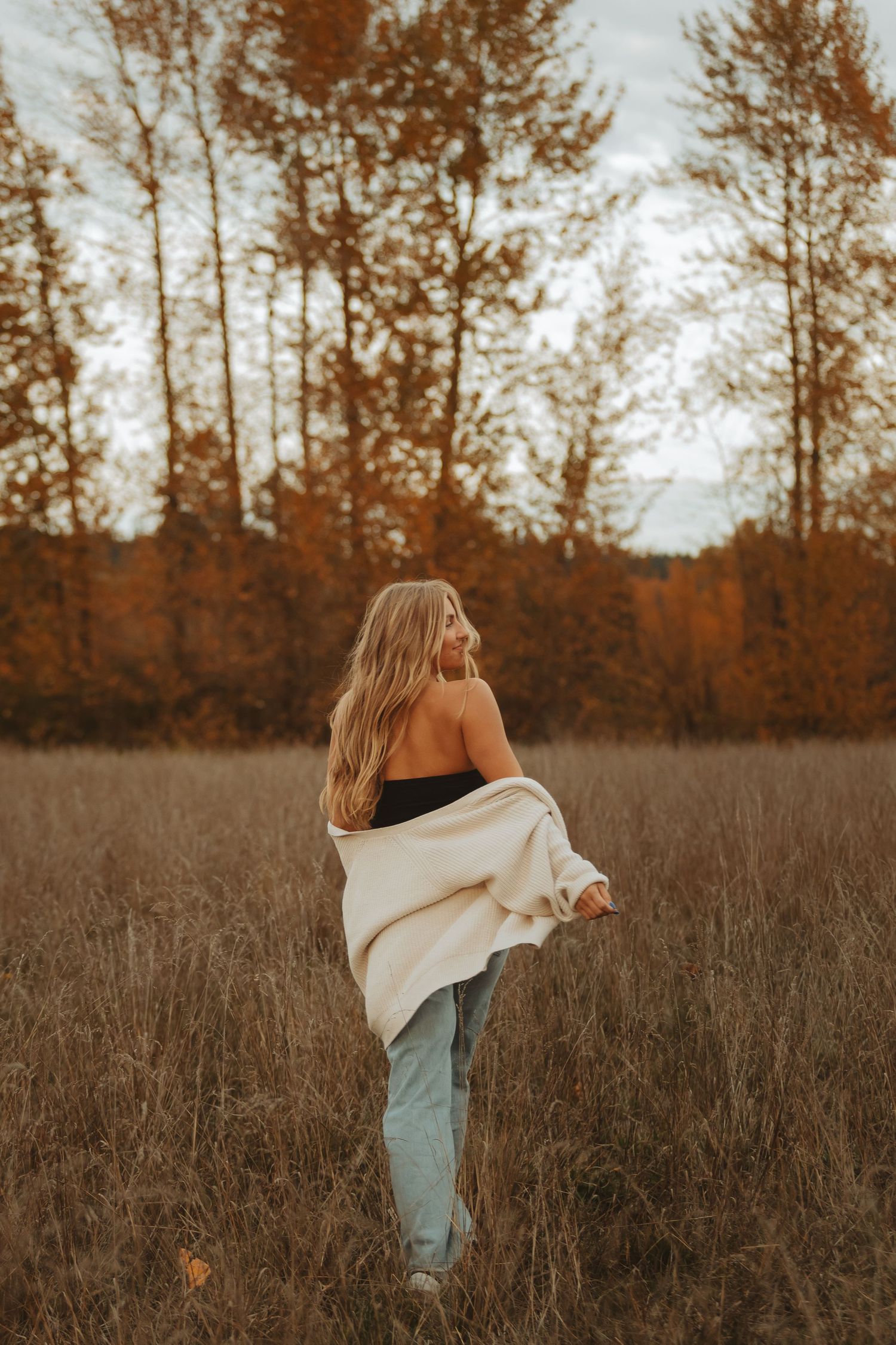 Figure dancing in a rustic field wearing denim and flowing white fabric during golden hour.