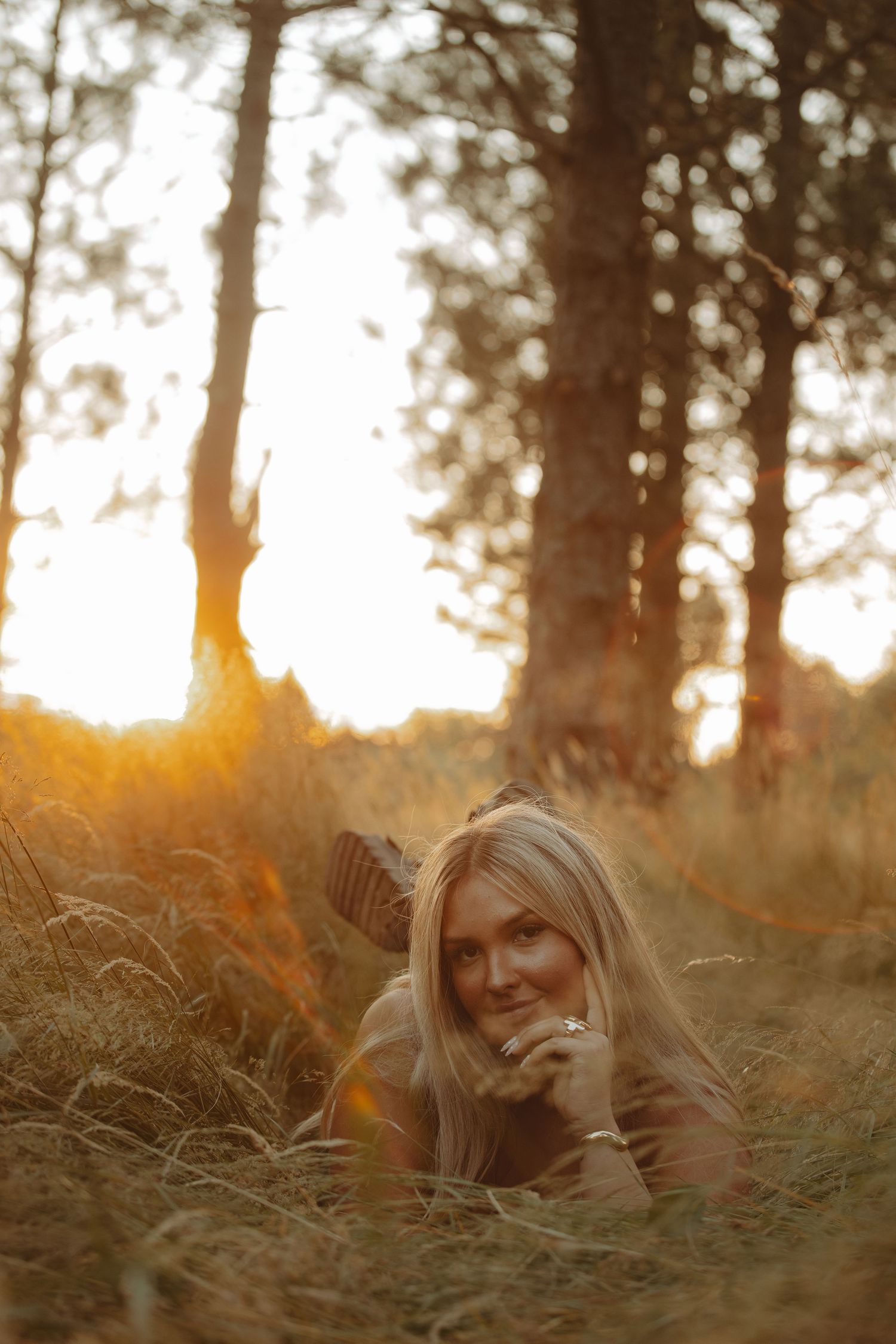 Artistic portrait lying in ferns with warm sunset light filtering through forest trees.