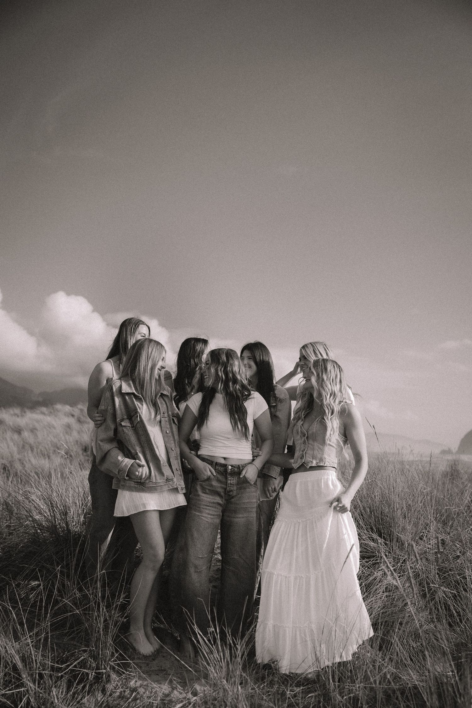 Black and white photo of five young women huddled together in a grassy field.