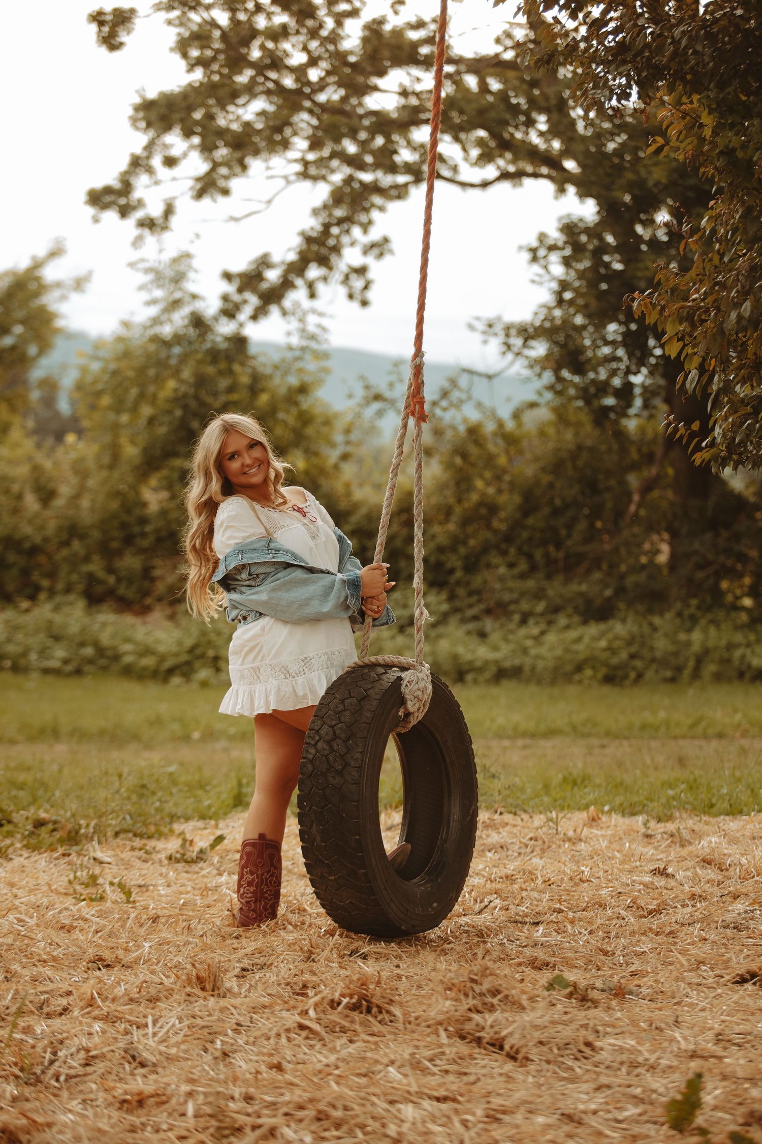 Person playing on an old tire swing in a rustic outdoor setting.