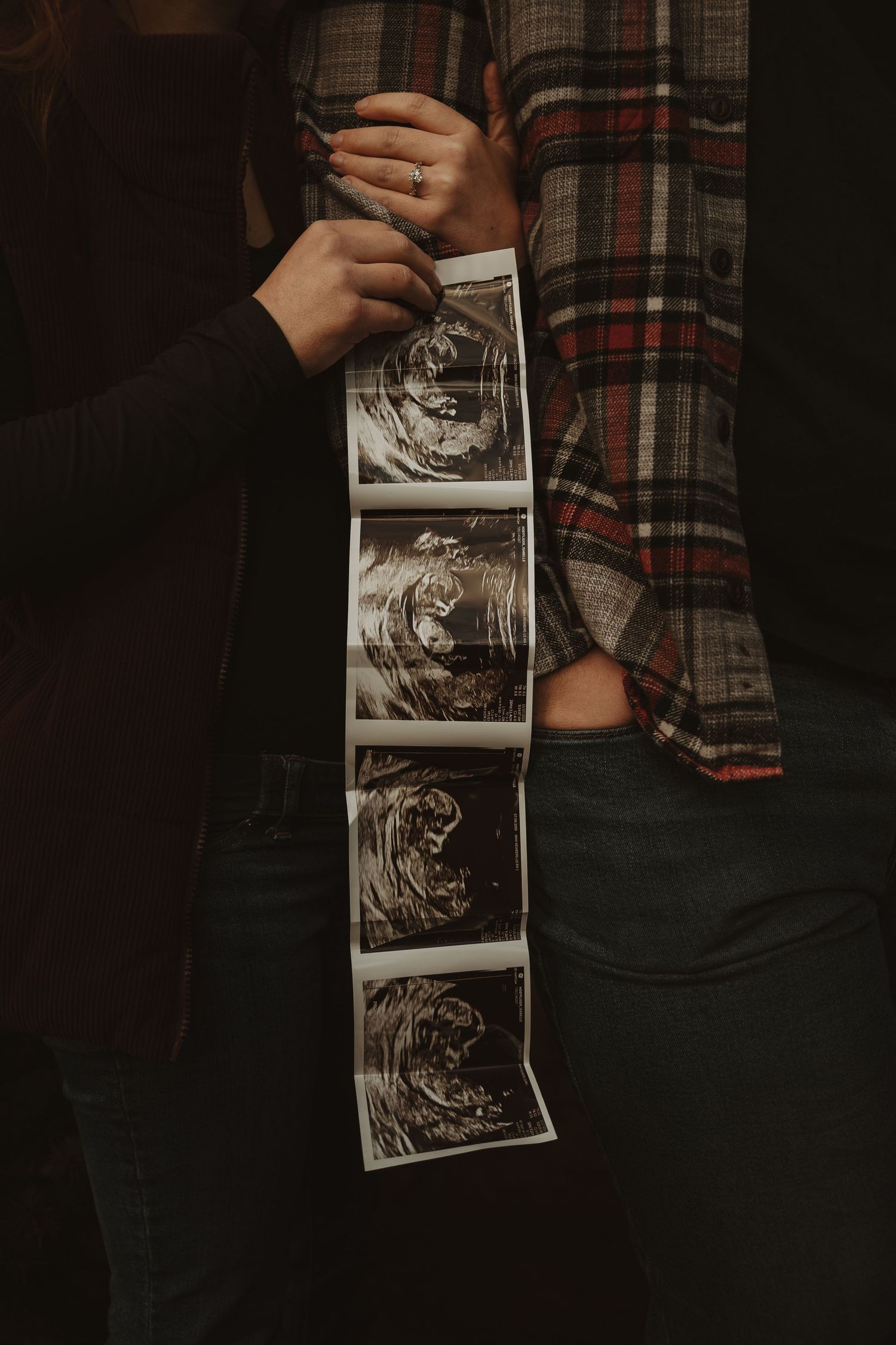 Someone holds a strip of ultrasound images showing the development of a baby in the womb against a dark background.