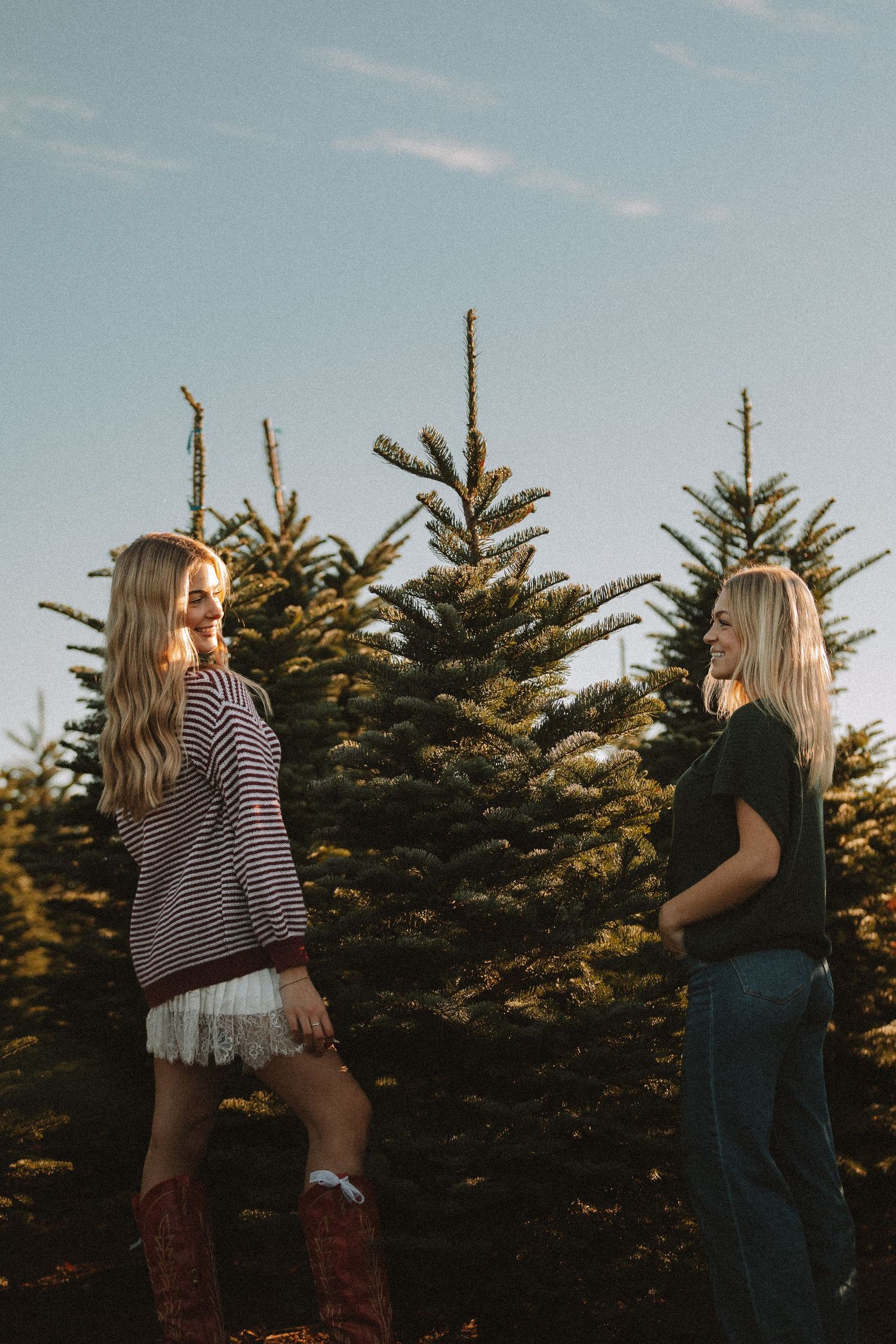 Friends enjoying a casual photoshoot among evergreen trees at sunset.