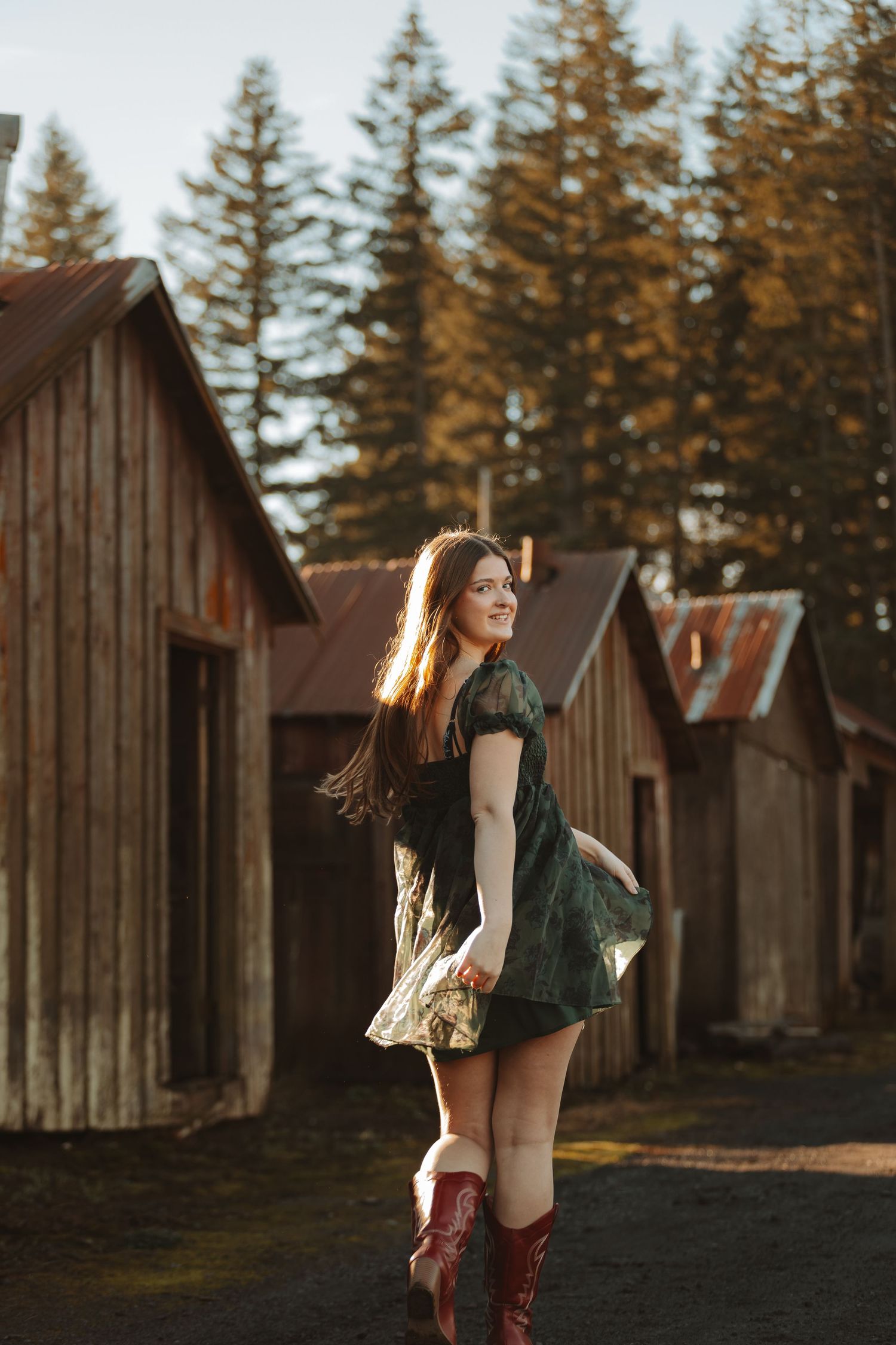 Silhouettes against sunset by wooden cabins with evergreen trees in background.