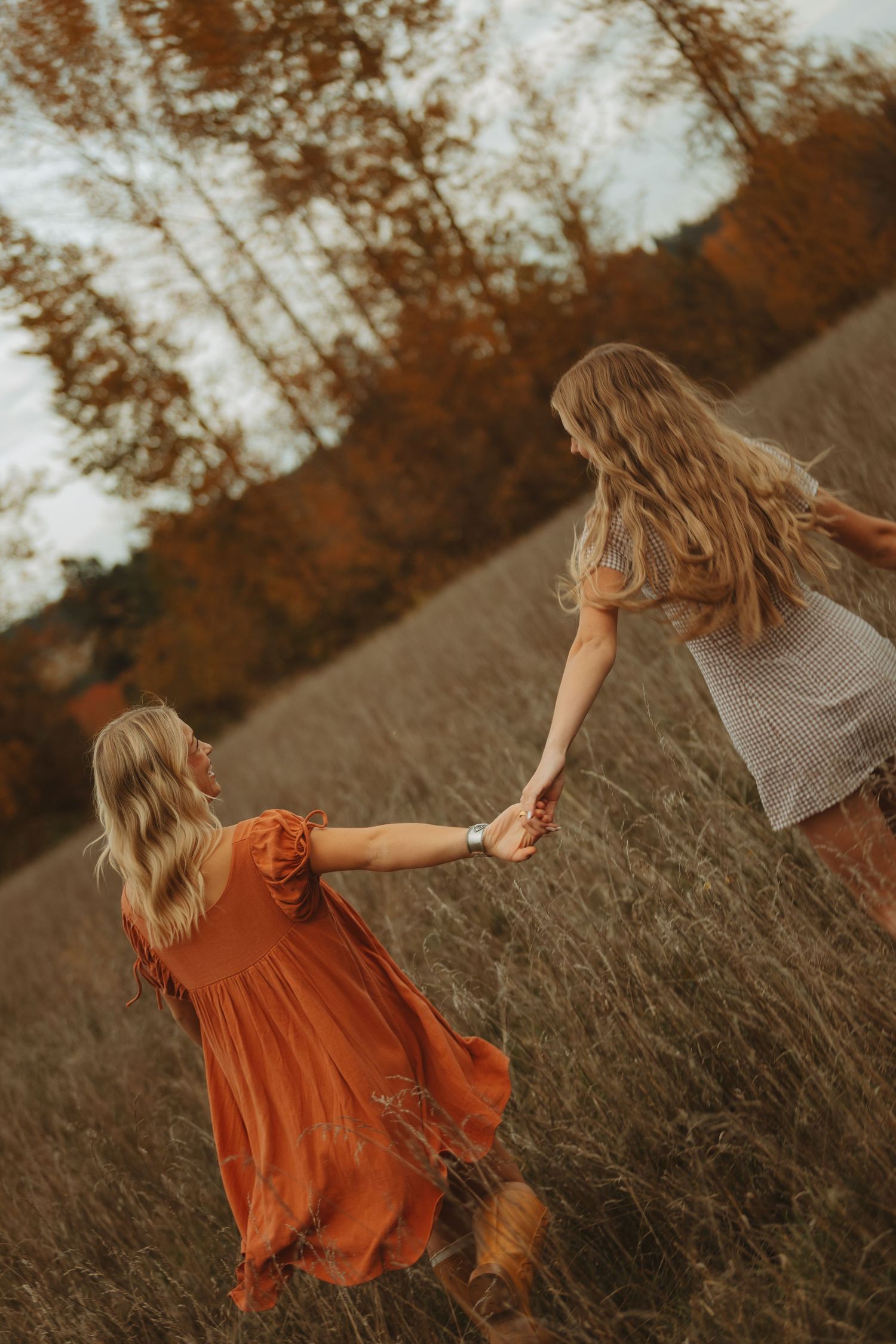 Two people hold hands while spinning through a golden field at sunset.