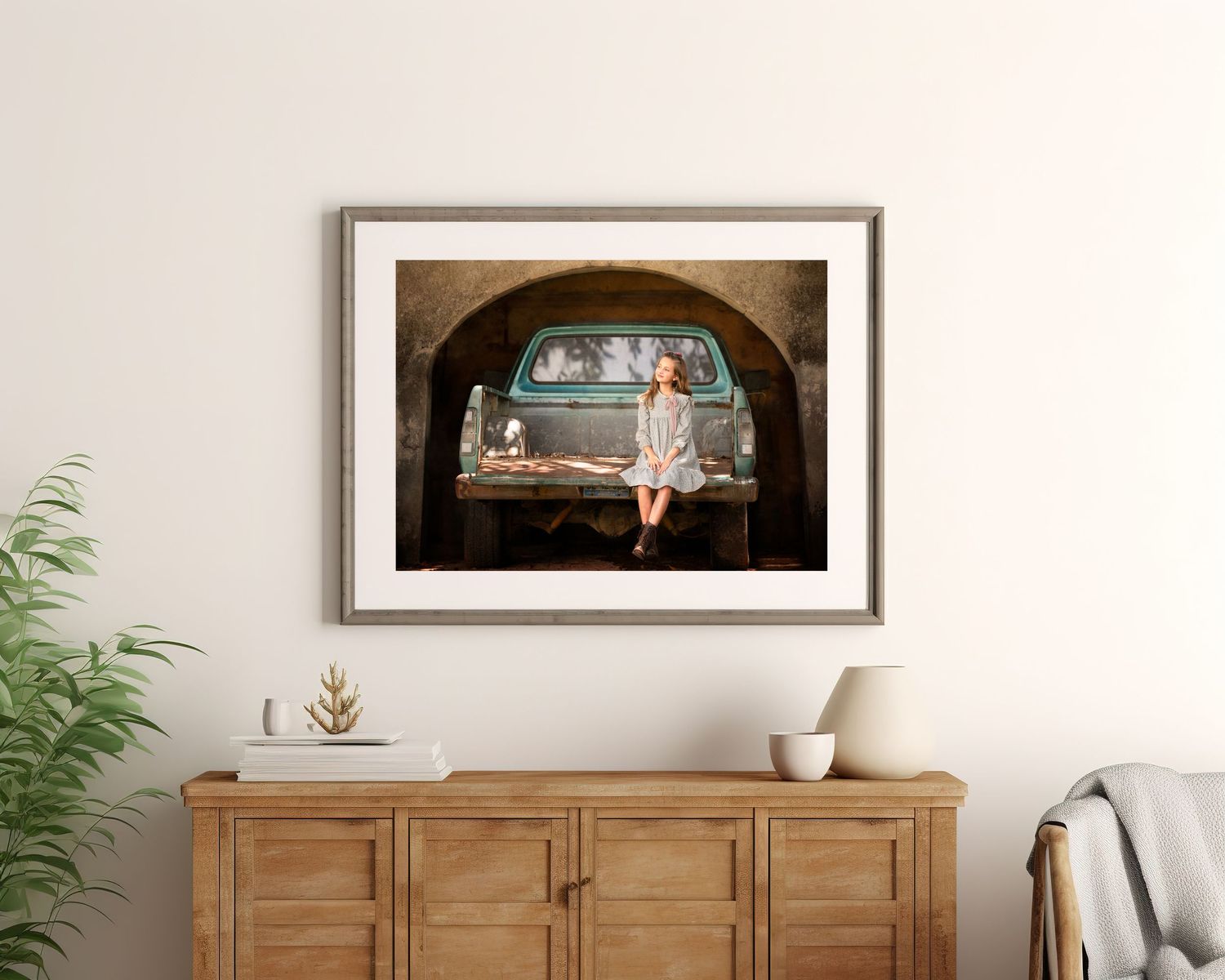 Vintage truck photo with little girl displayed in wooden frame above rustic sideboard with minimalist decor.