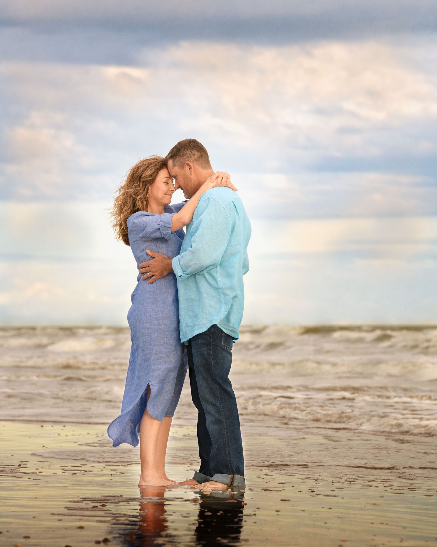 Romantic couple embracing on a beach at sunset with waves in the background.