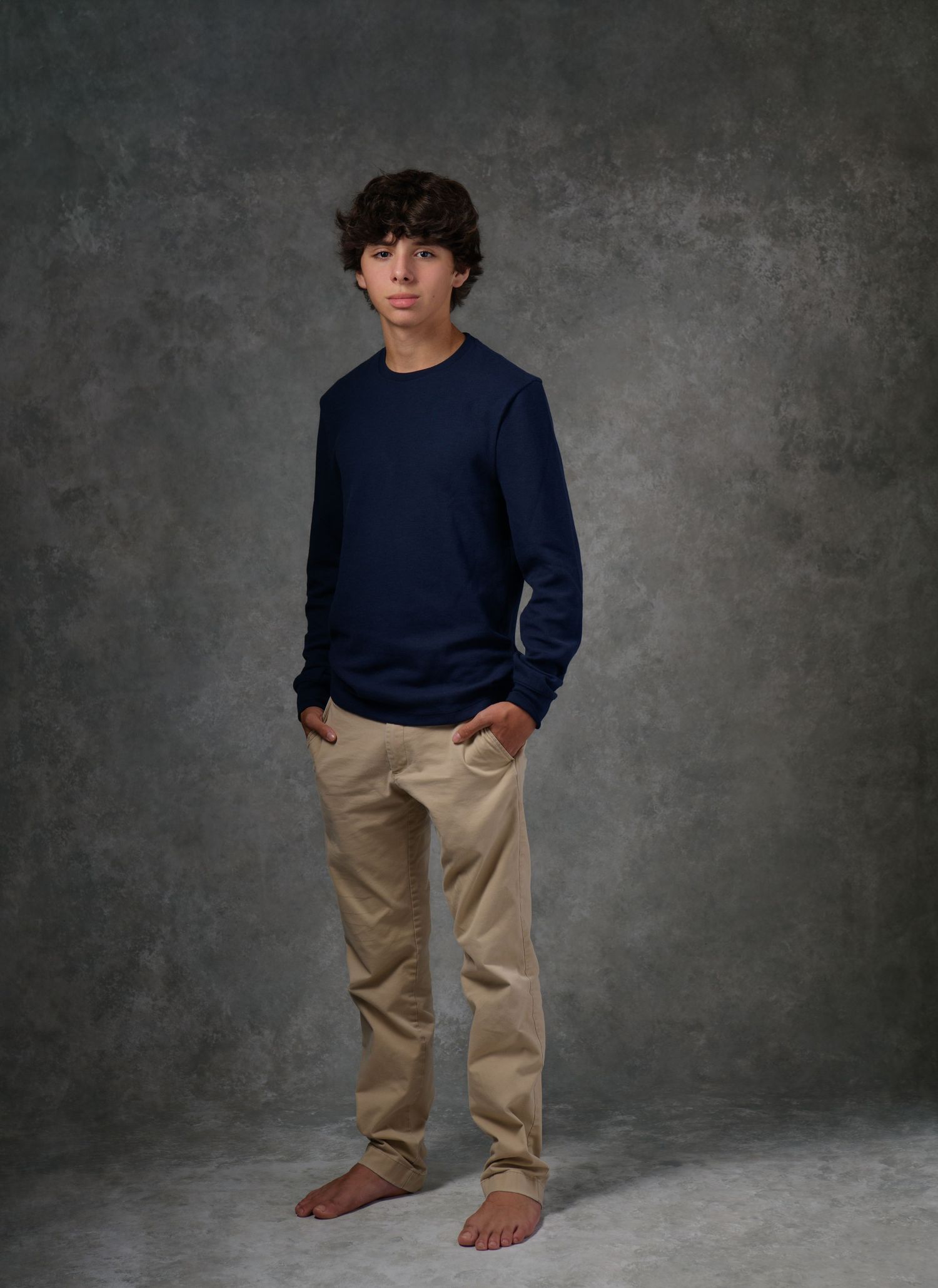 Studio portrait of teenager in navy sweater and khaki pants against grey background.