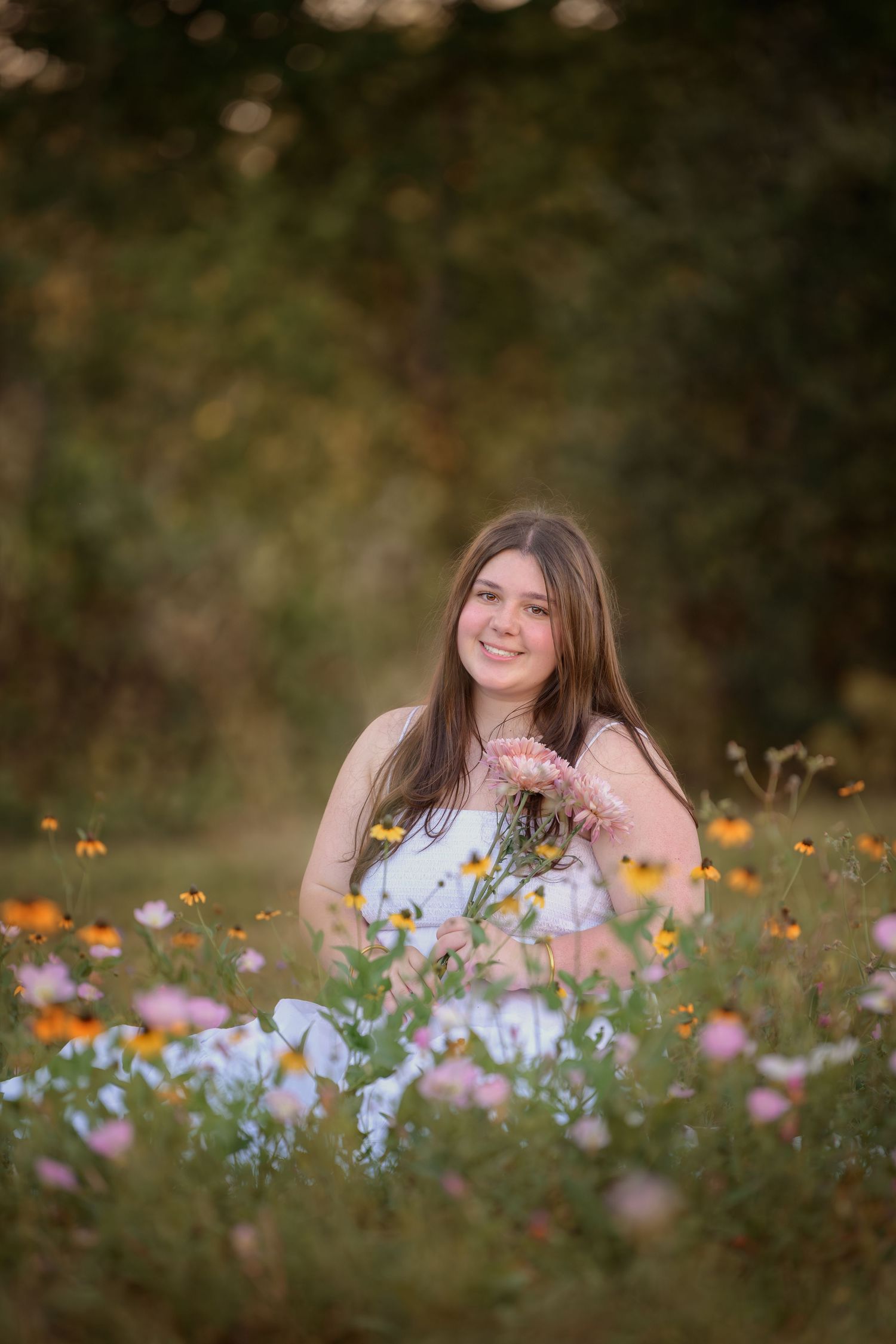 A young woman in a blue dress sits in a wildflower meadow during golden hour with colorful blooms all around.