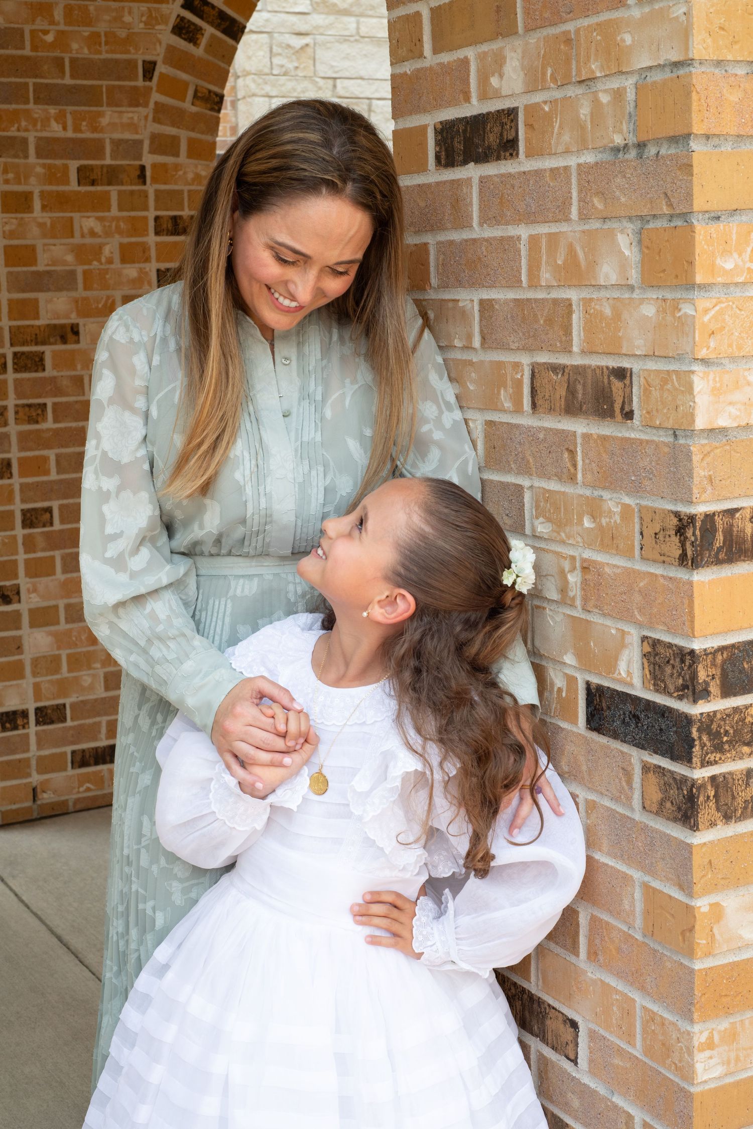 A heartwarming interaction between mom and daughter by a brick archway.