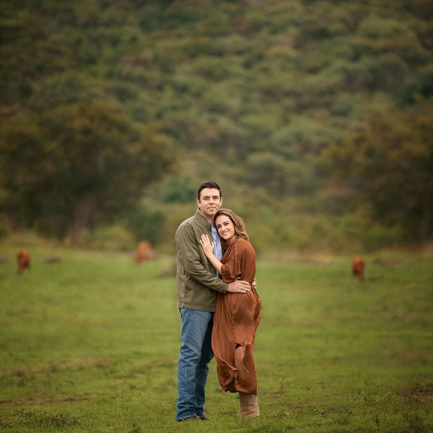 Couple embracing in rural field with green hills in background.
