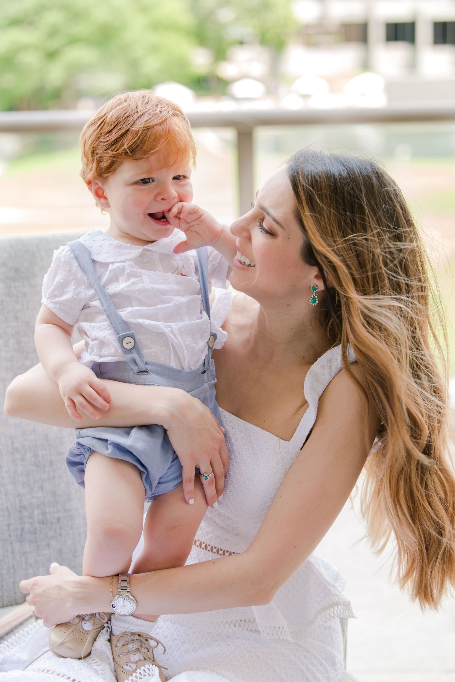 Tender moment between parent and toddler sitting on grey sofa outdoors.