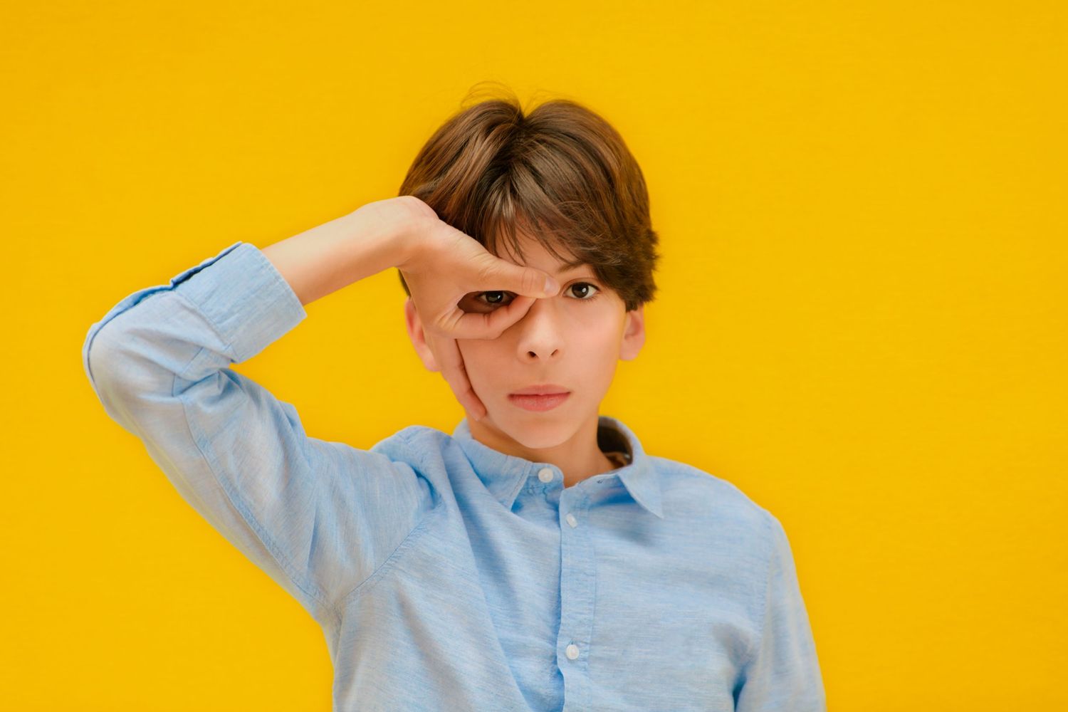 Boy in light blue shirt making silly face against bright yellow background.