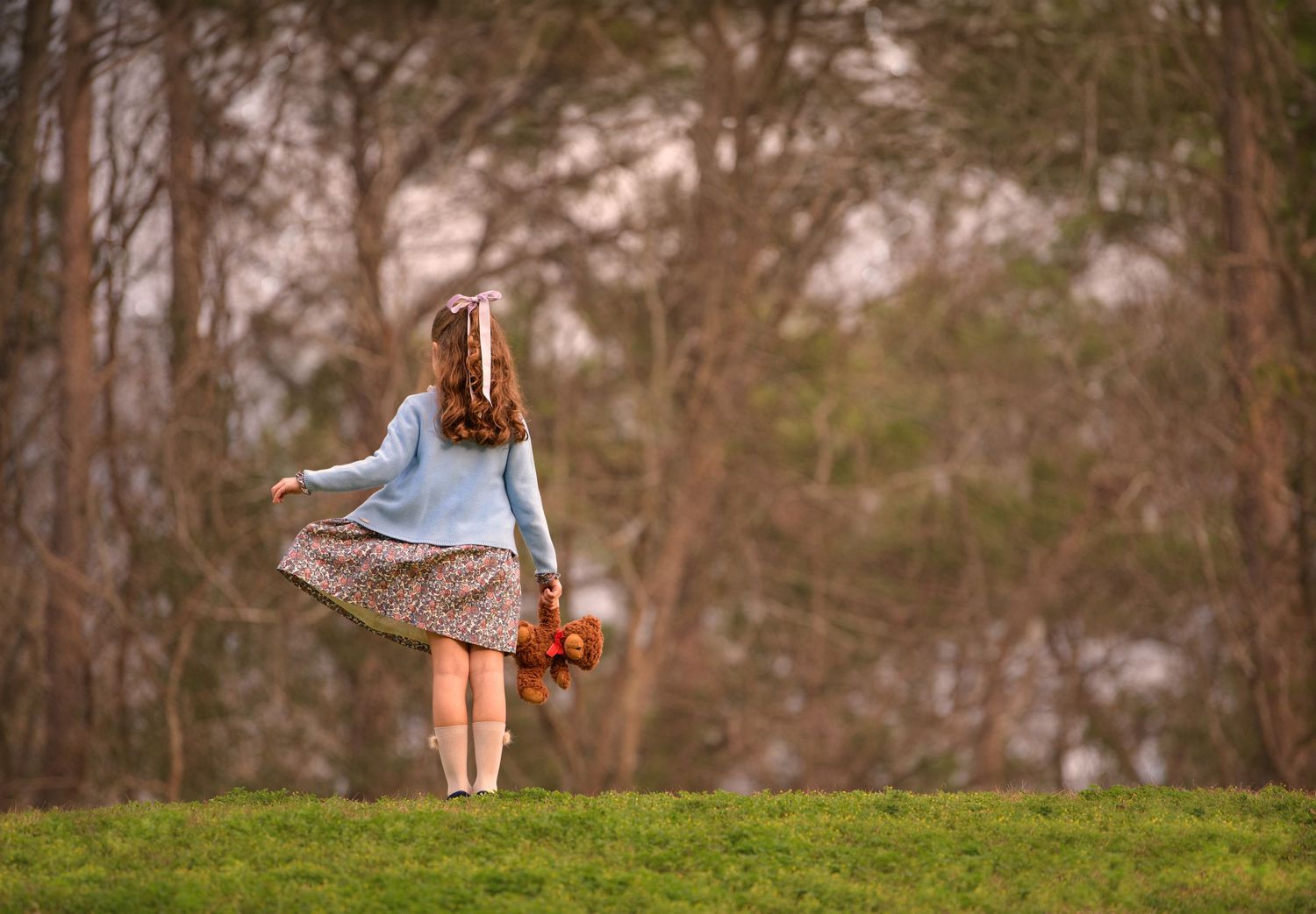 Child in blue sweater twirling in a dress while holding flowers in an autumn field.