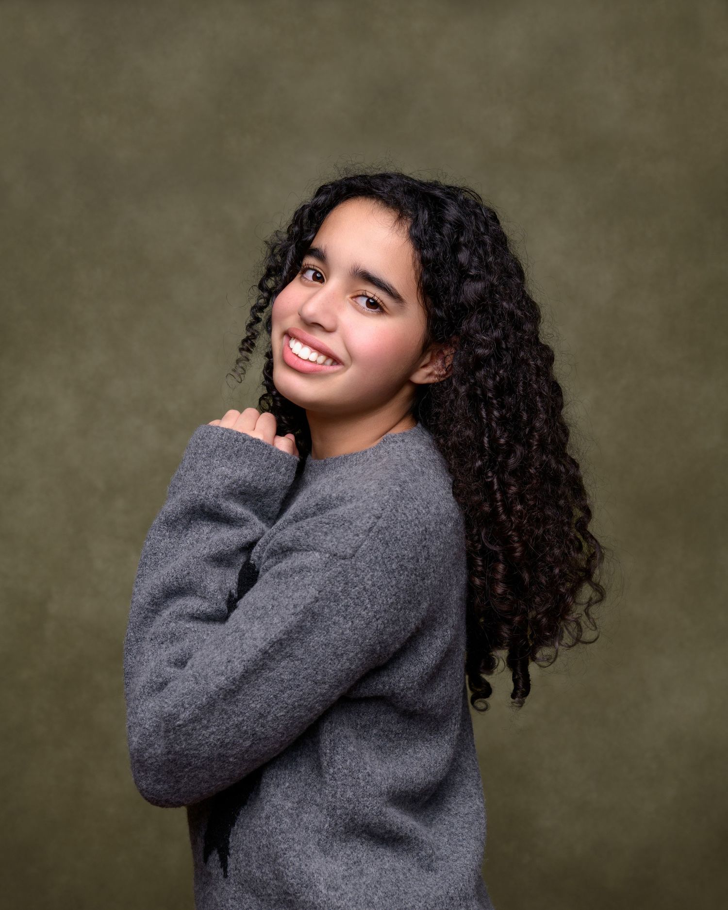 A person in a cozy grey sweater poses playfully against a dark background in a four-panel portrait series.