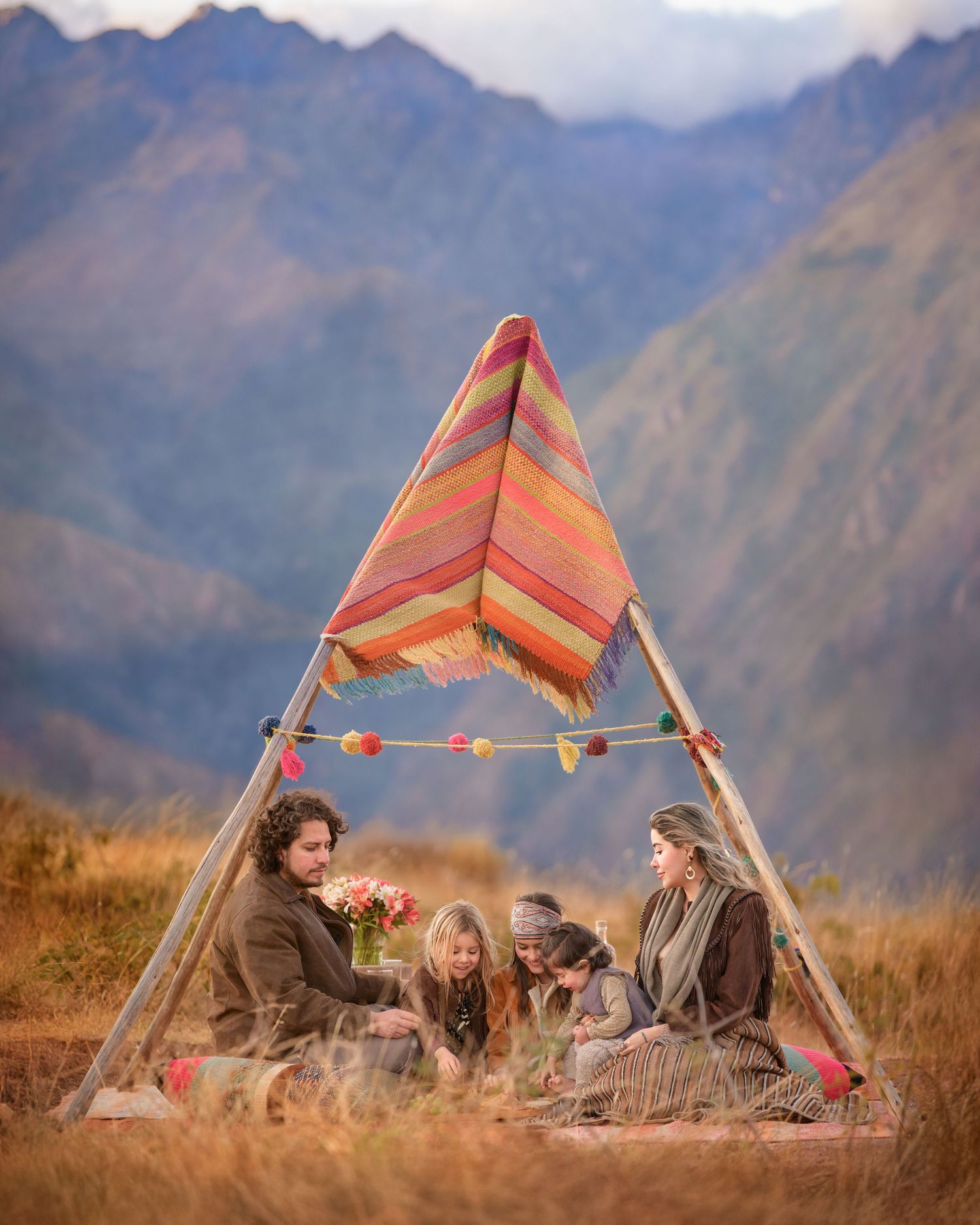 A colorful triangle tent shelter with string lights set against majestic mountain peaks during golden hour.
