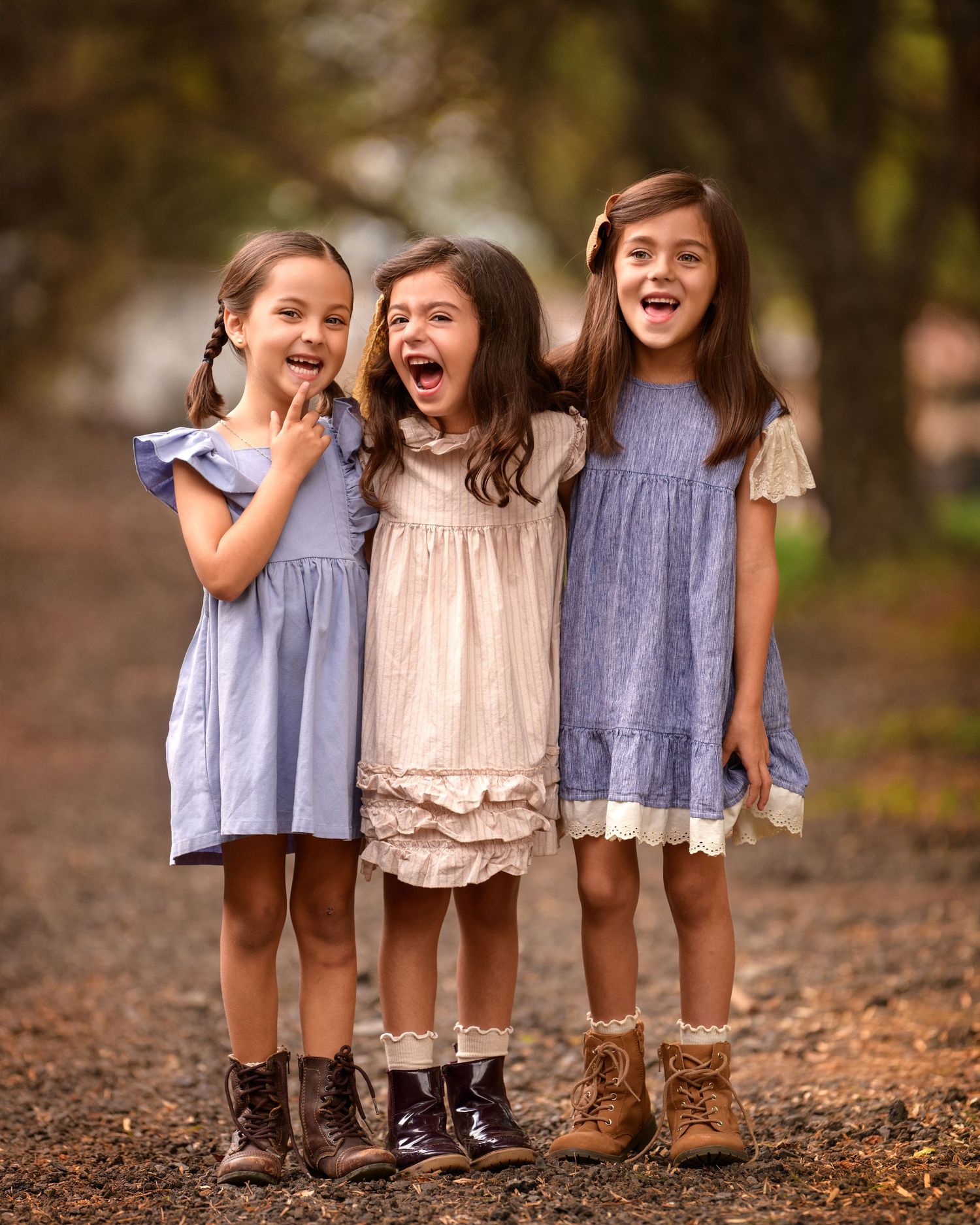 Three children wearing casual dresses and boots stand together laughing on fallen autumn leaves.