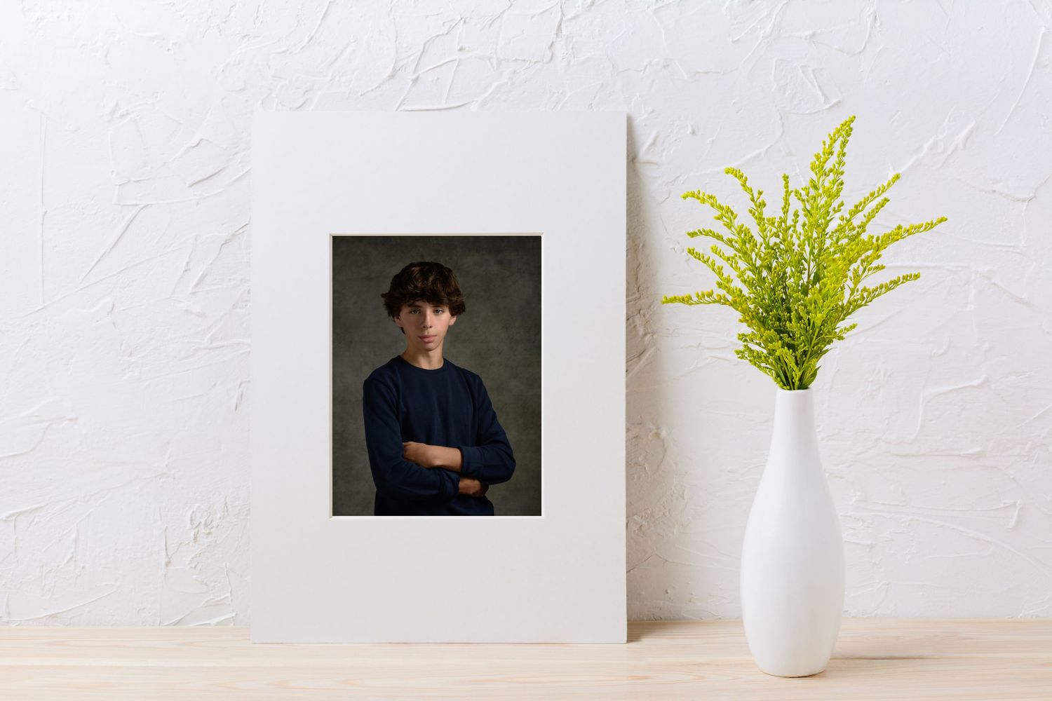 Studio portrait displayed in white frame with green plant in modern vase.