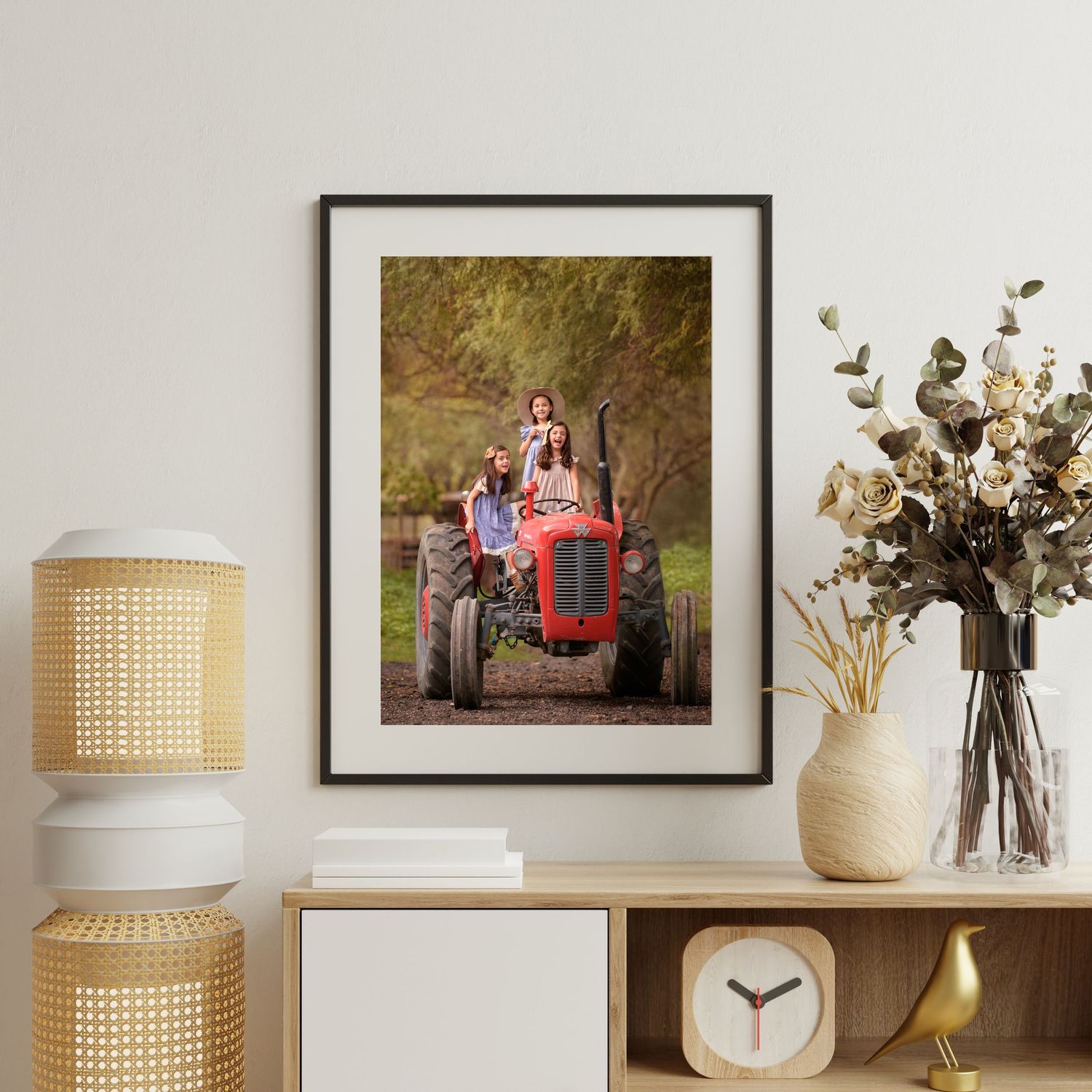 Framed photograph of vintage red tractor displayed on wooden shelf with decorative items and table lamp.