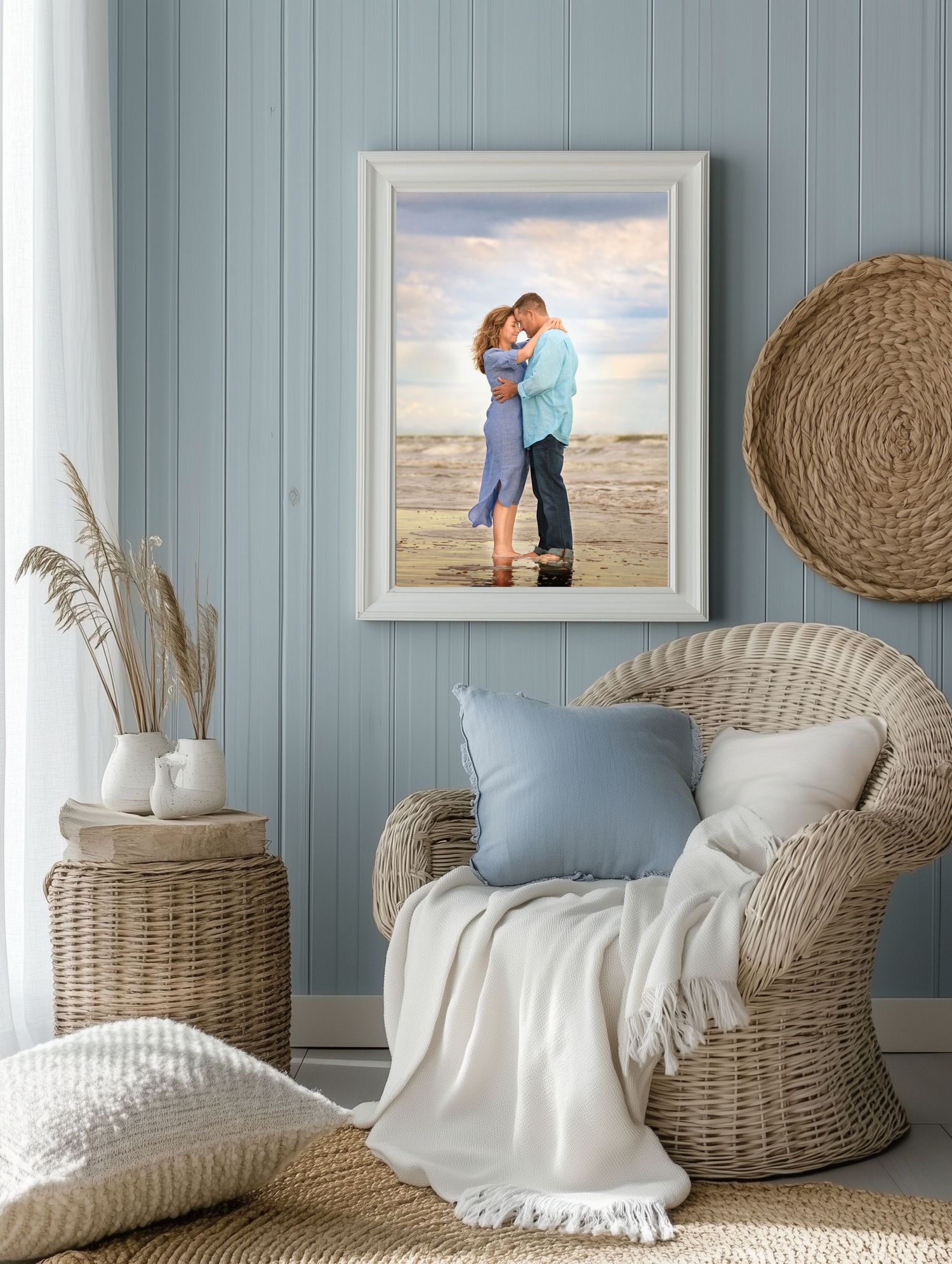 A framed beach couple's photograghy displayed on blue paneled wall with wicker chair and coastal decor.
