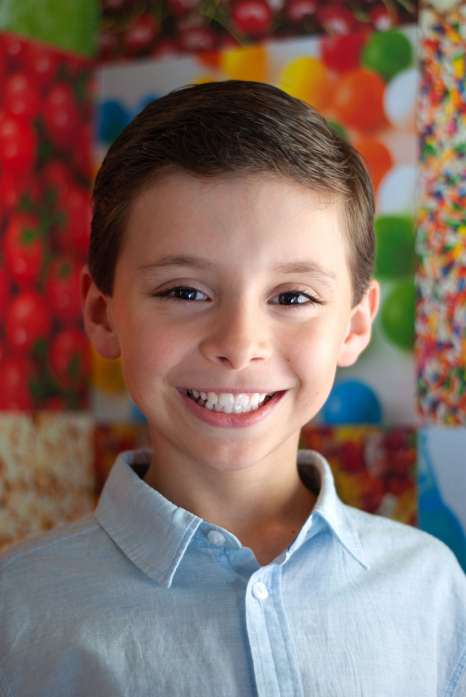 Portrait of boy against colorful festive background wearing light blue collared shirt.