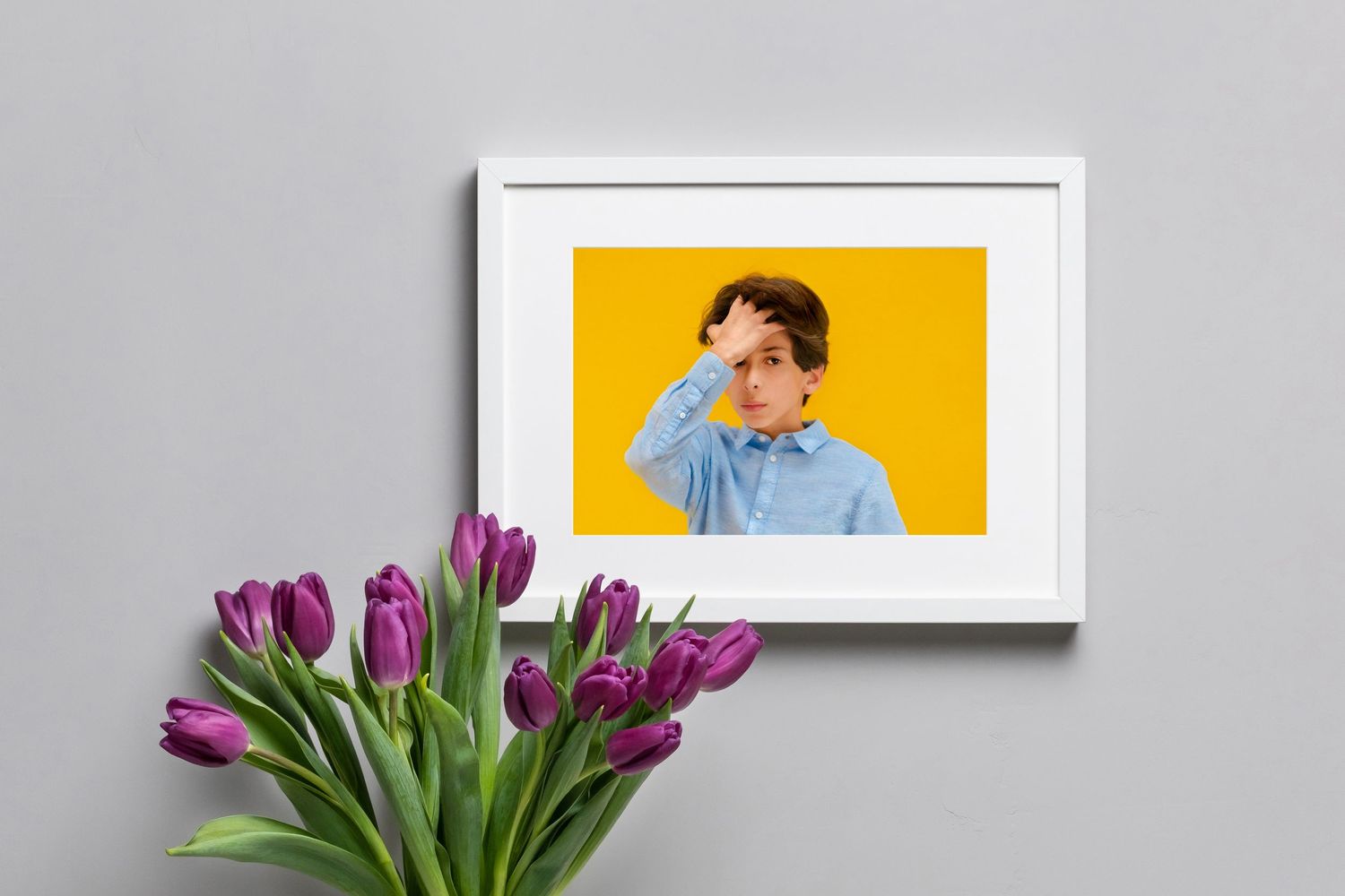 White framed portrait of boy against yellow background with purple tulips in foreground.