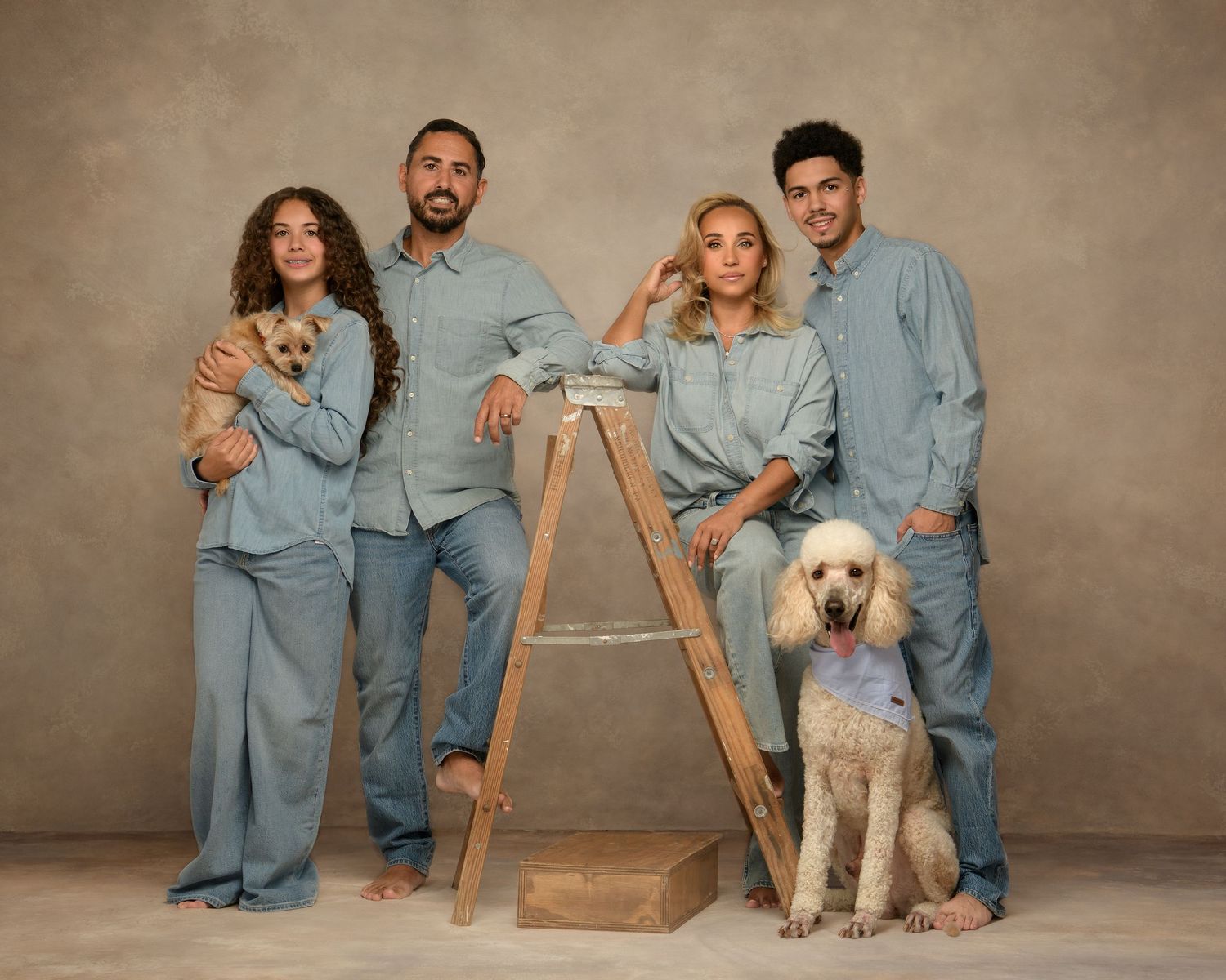 Family in matching denim outfits poses for a series of casual studio portraits with their golden retriever dog.