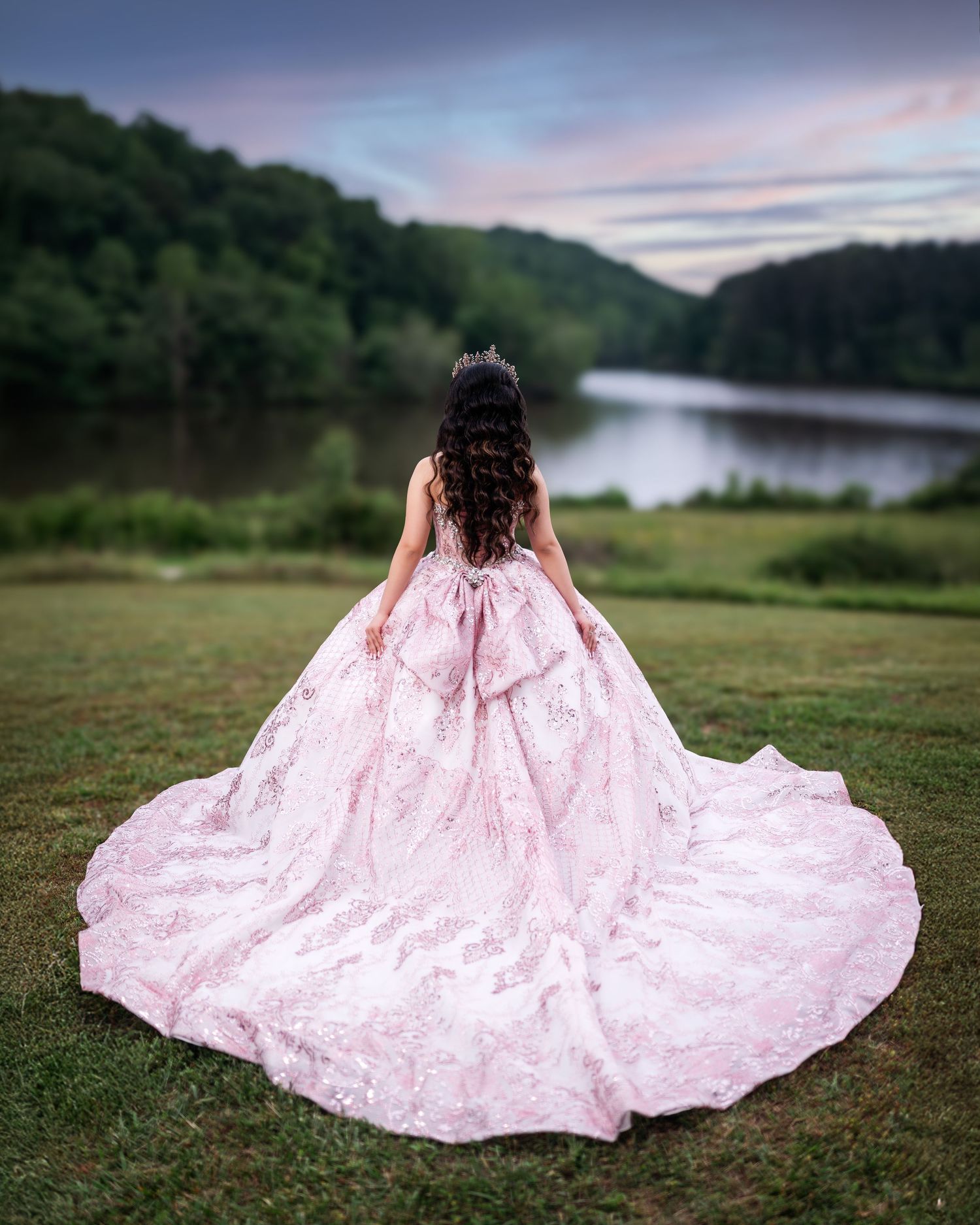 A dramatic back view of a pink princess ball gown with cathedral train beside a lake.