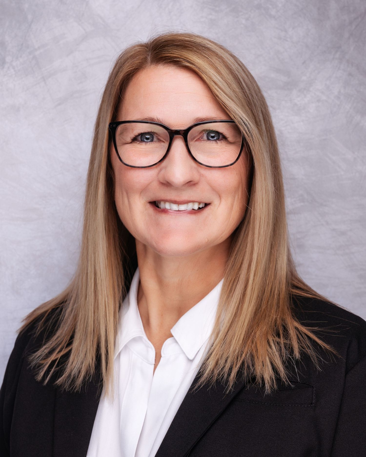 Professional portraits of person in black blazer and white button-up shirt with glasses.