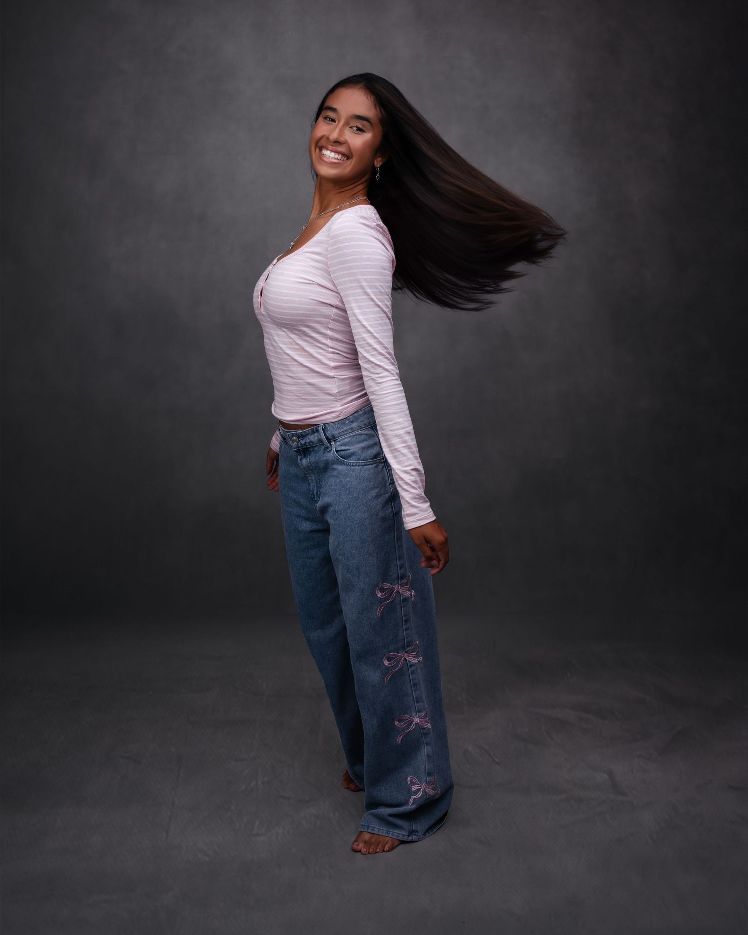 Woman in white long sleeve top and embroidered jeans poses dynamically against dark backdrop in studio setting. Buford GA