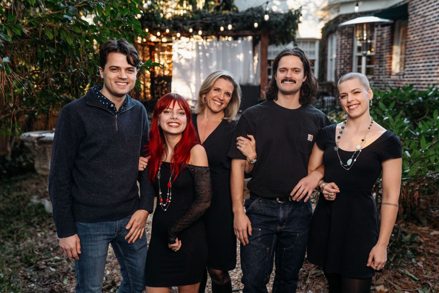 Family gathering on front porch wearing coordinated black outfits for holiday photos.