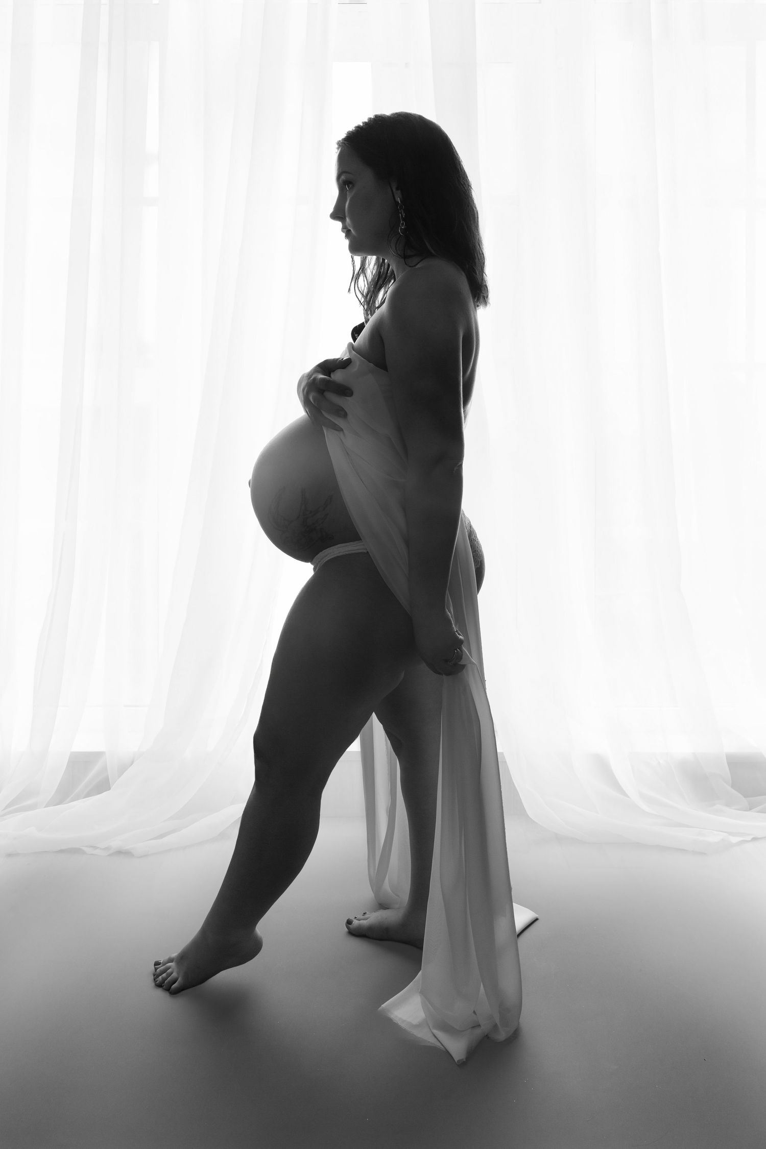 Black and white silhouette maternity photos with flowing fabric and dramatic lighting.