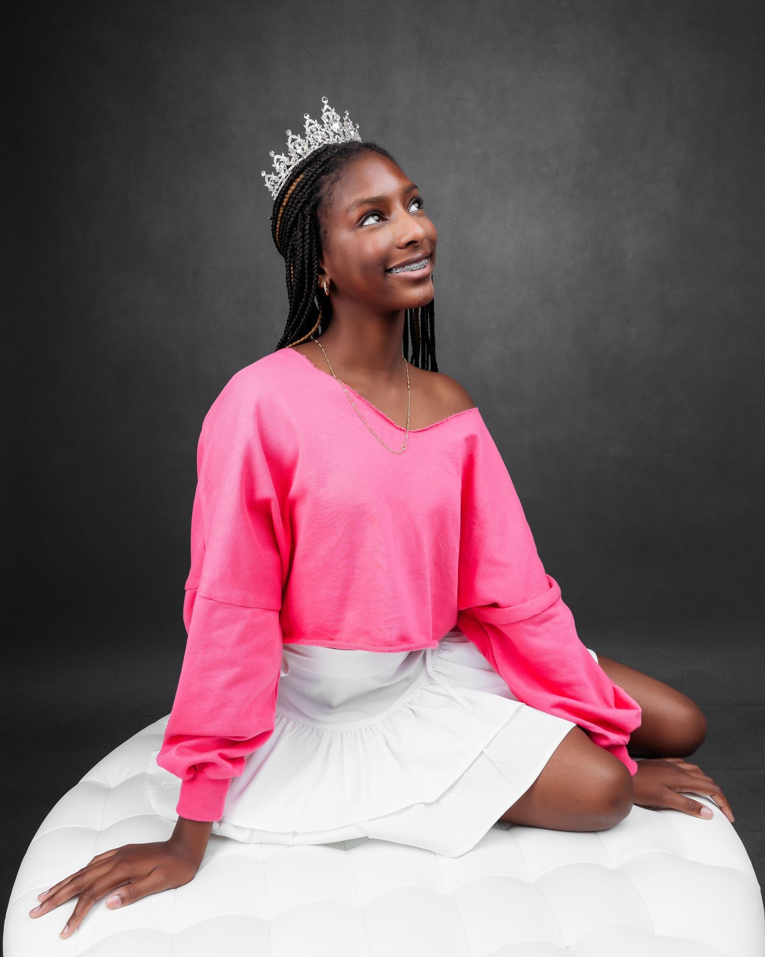 Studio portrait of someone wearing a bright pink top and white skirt against a dark background.