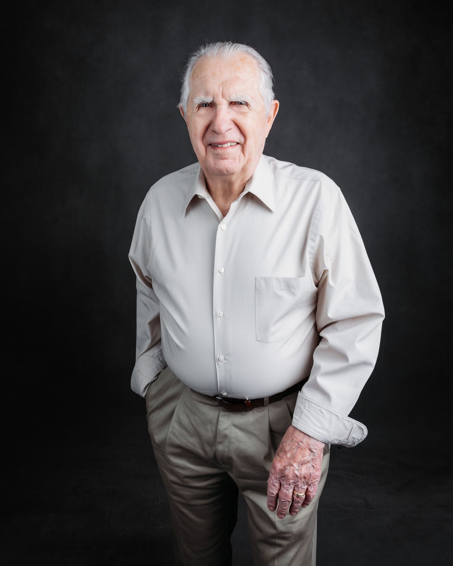 Portrait of senior in white shirt and khakis against dark studio backdrop.