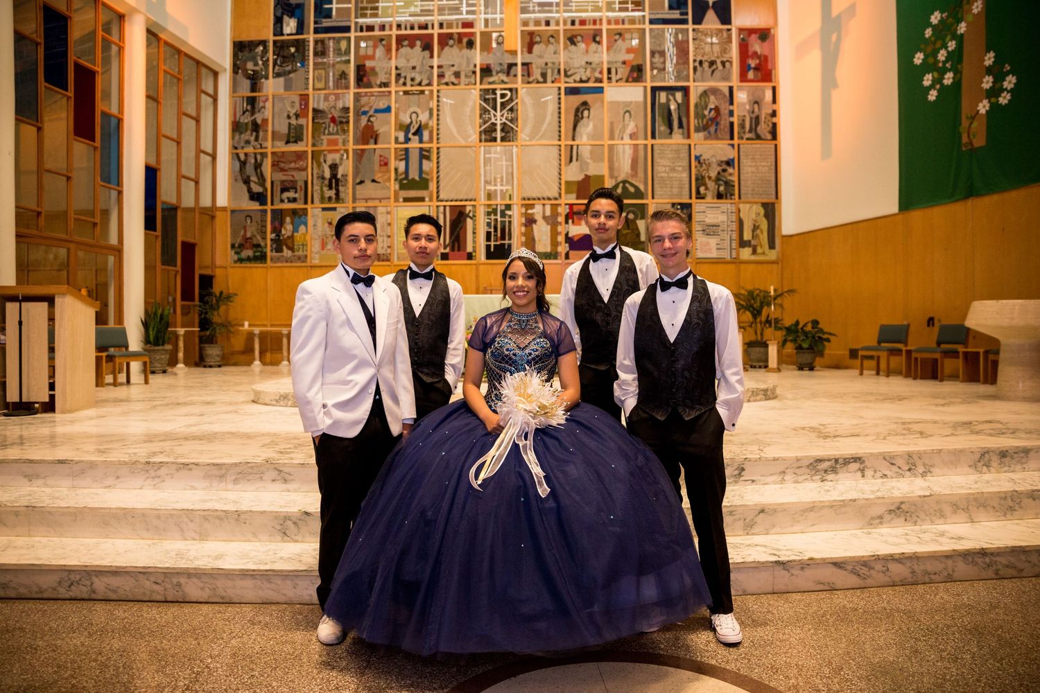 Wedding party poses together in front of a decorative wall display with photos.
